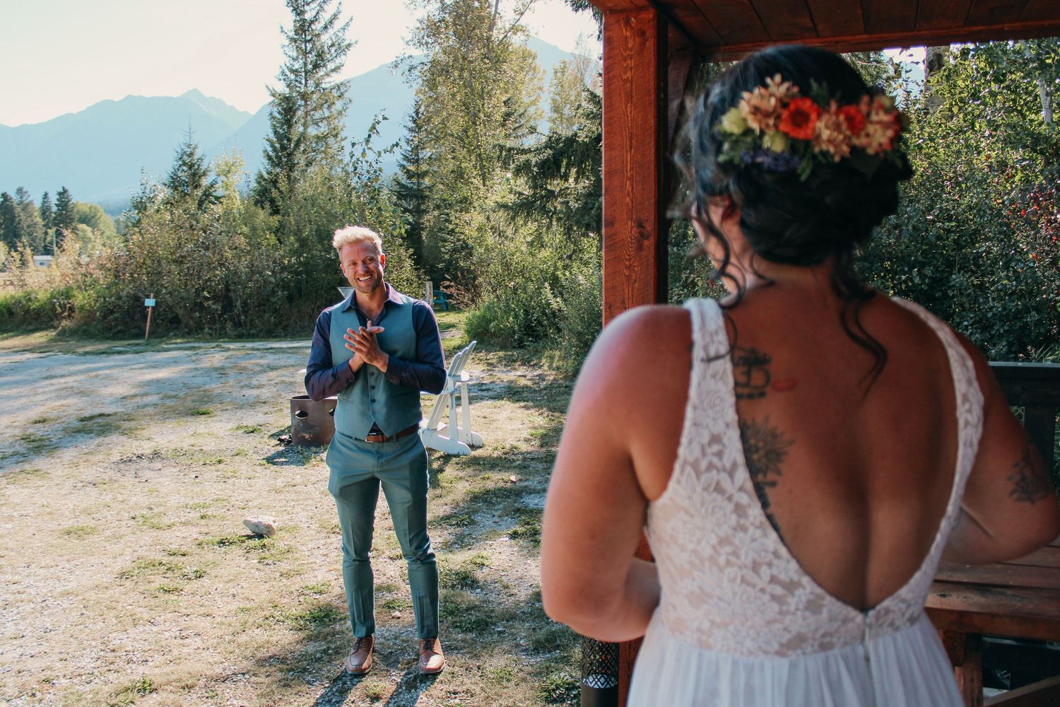 Intimate wedding scene with couple embracing beneath wooden beams against mountain landscape.