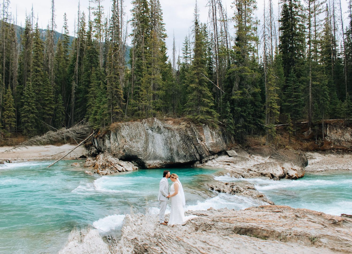 Stunning turquoise mountain river flows through rocky terrain surrounded by pine trees.