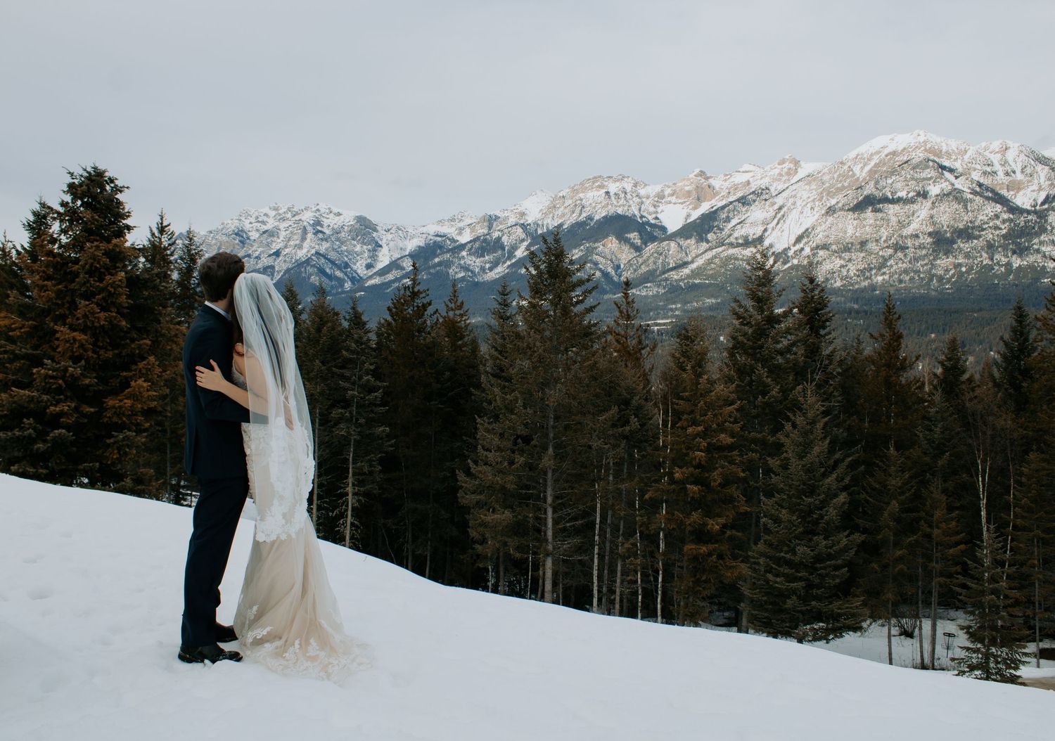 A couple shares a romantic moment during their winter wedding photoshoot in a snowy mountain landscape.