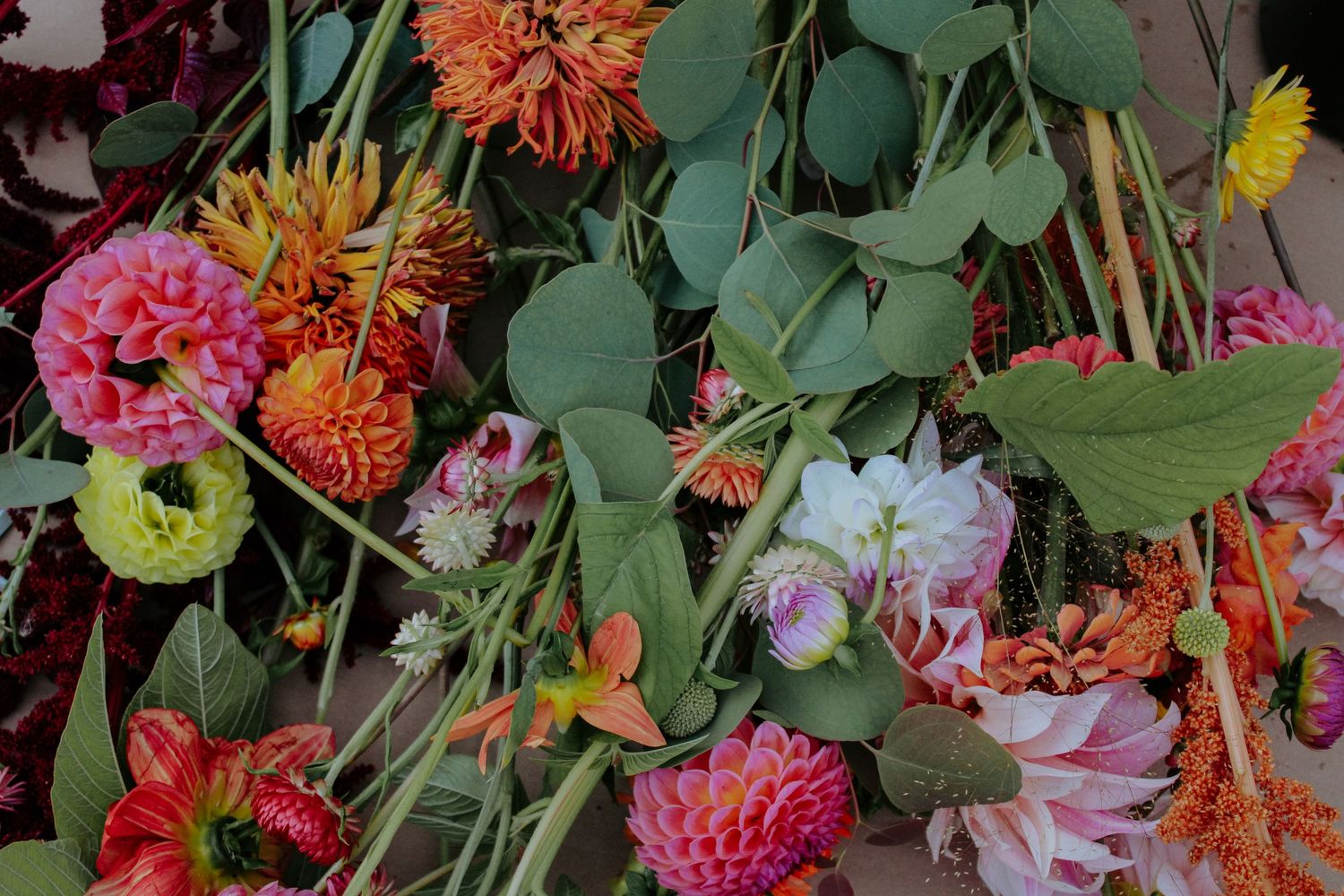 Assorted dahlias and wildflowers in bright pink, orange and yellow arranged on a light surface.
