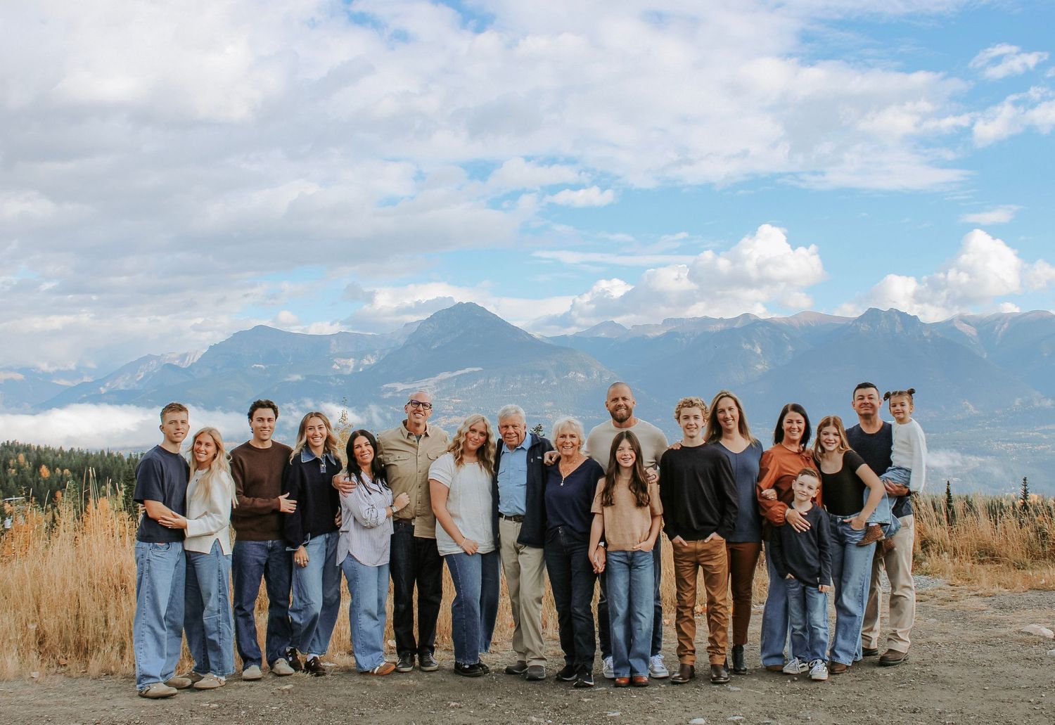Large group portrait against a scenic mountain backdrop with blue sky and clouds.