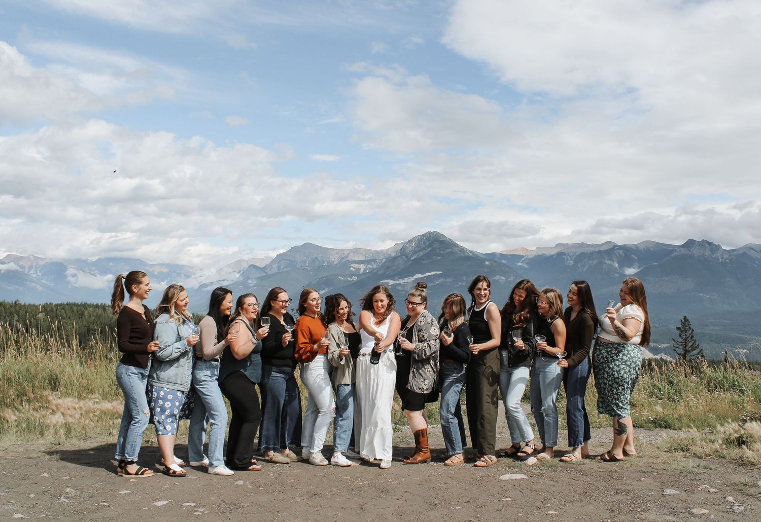 Group of women posing together outdoors with stunning mountain and cloudy sky backdrop in a scenic location.