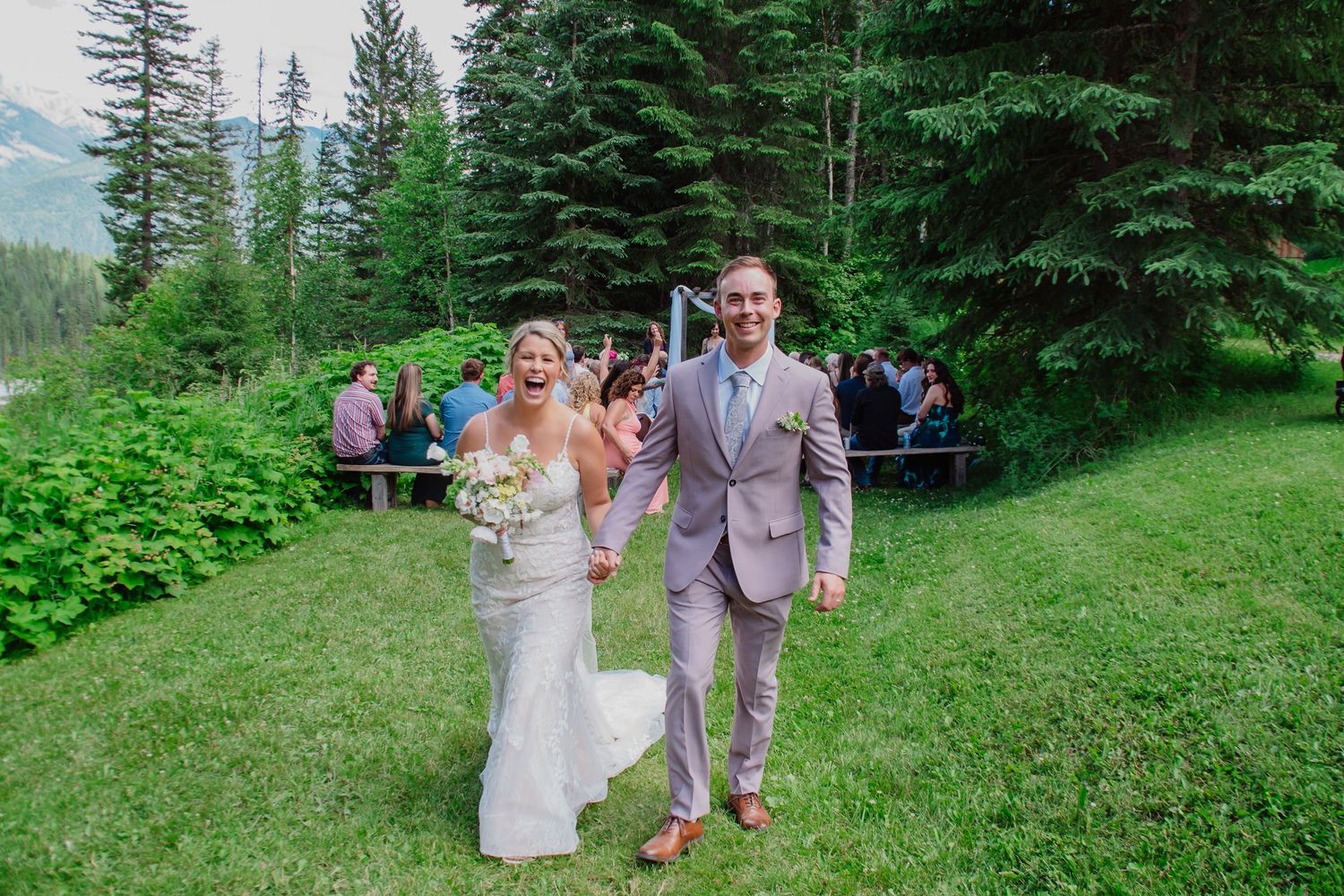 Joyful bride and groom walking down the aisle after outdoor mountain wedding ceremony.