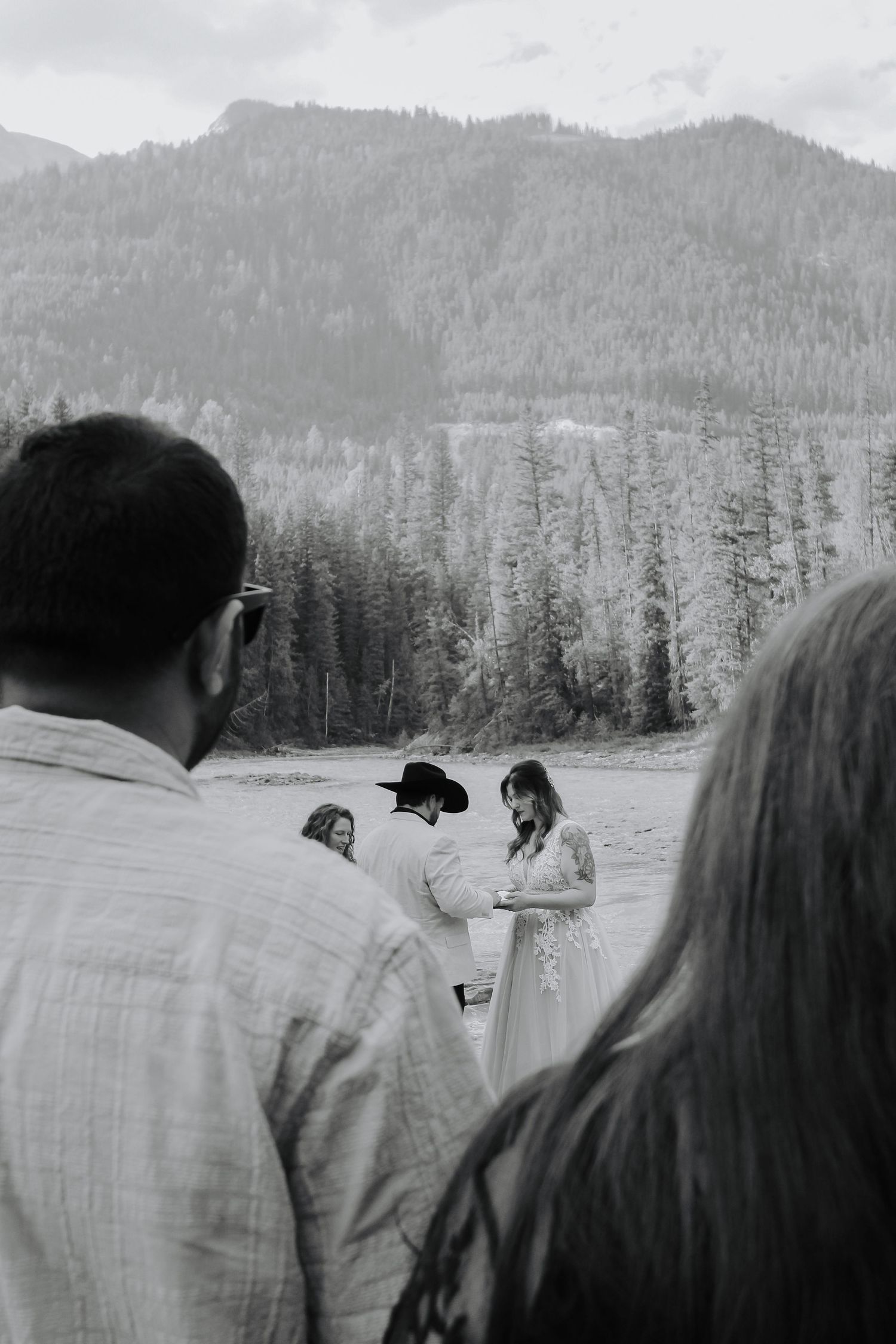 Black and white outdoor wedding ceremony with mountains and pine trees in the background.