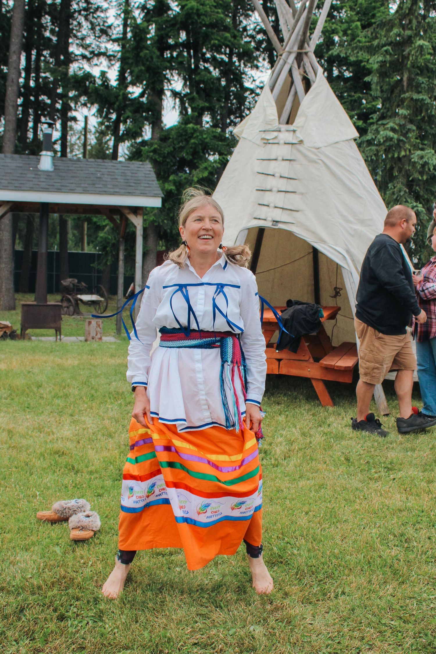 Woman in traditional Indigenous regalia dances outdoors near a white teepee at a cultural gathering.