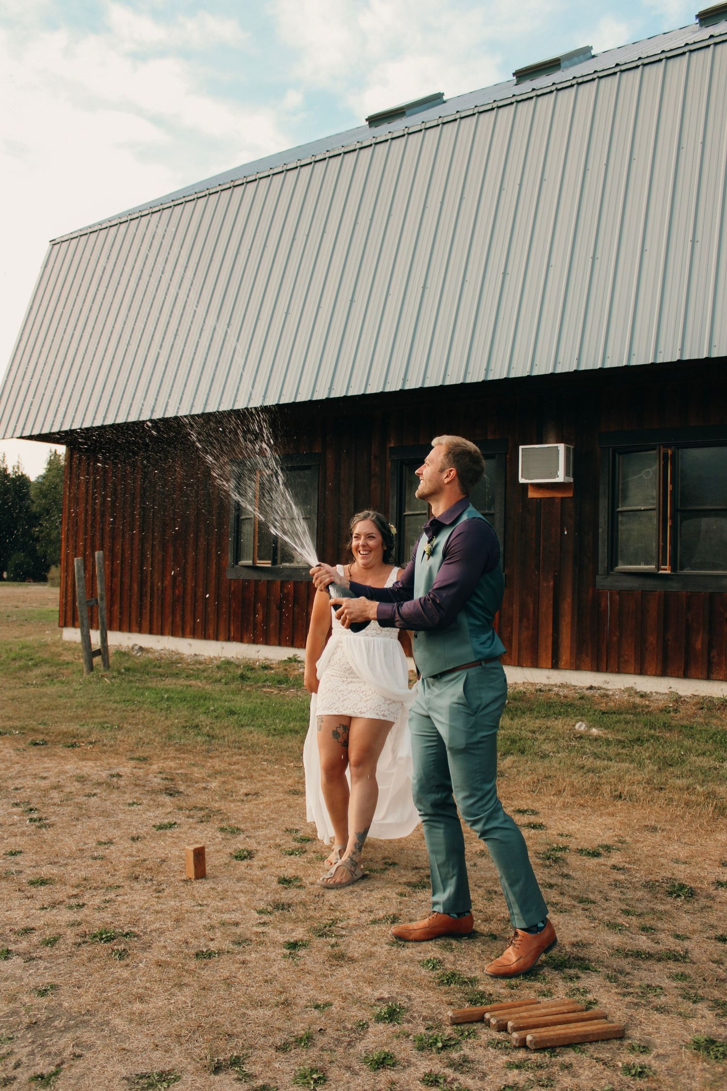 Wedding couple plays a fun game outside a rustic building with metal siding.