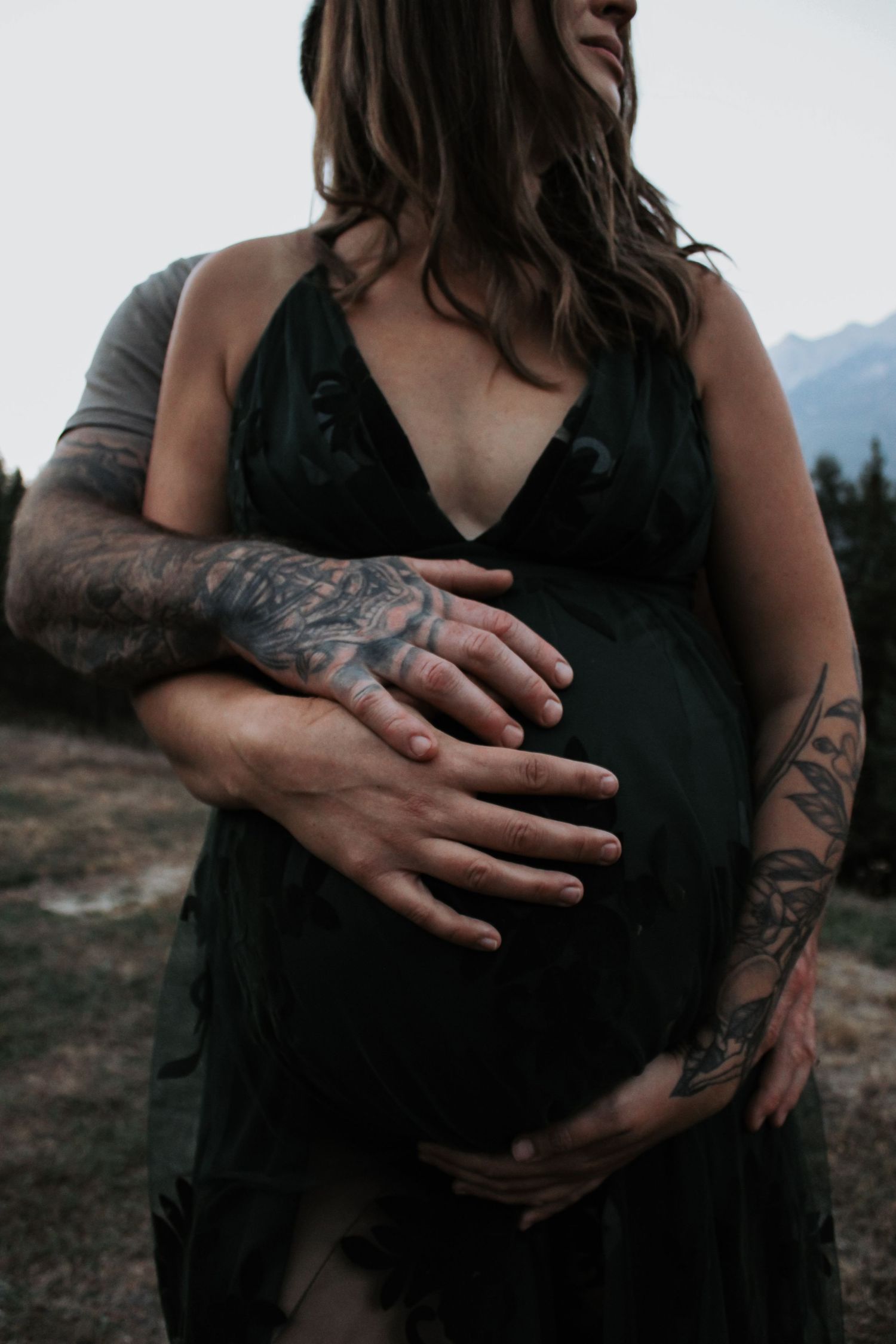 Close-up of tattooed arms embracing in an intimate outdoor portrait.