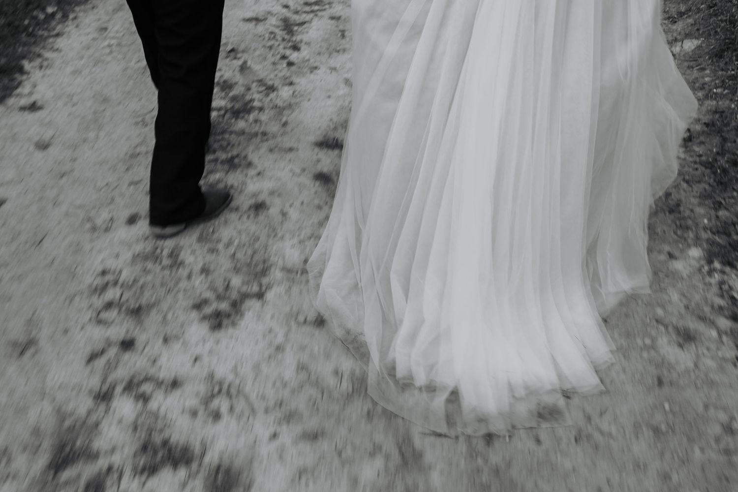 Black and white photo of a bride in a flowing white gown standing on snowy ground beside a groom in dark attire.