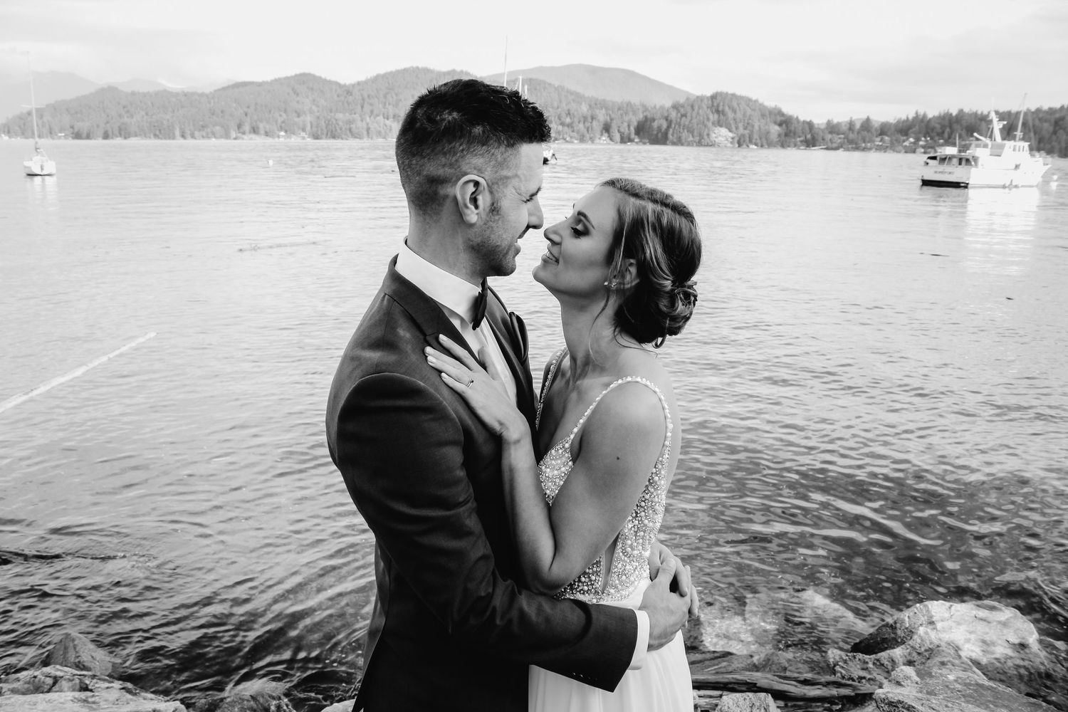 Romantic black and white photos of a couple embracing by a lake with mountains in the background.
