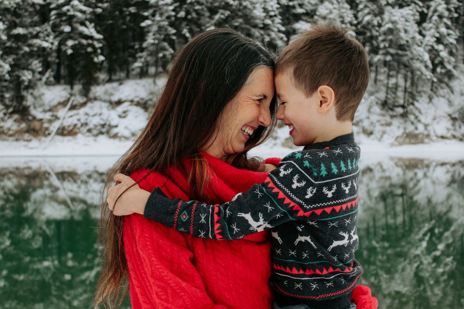 A tender moment shared between two people wearing festive winter sweaters against a snowy landscape lifestyle family photography session