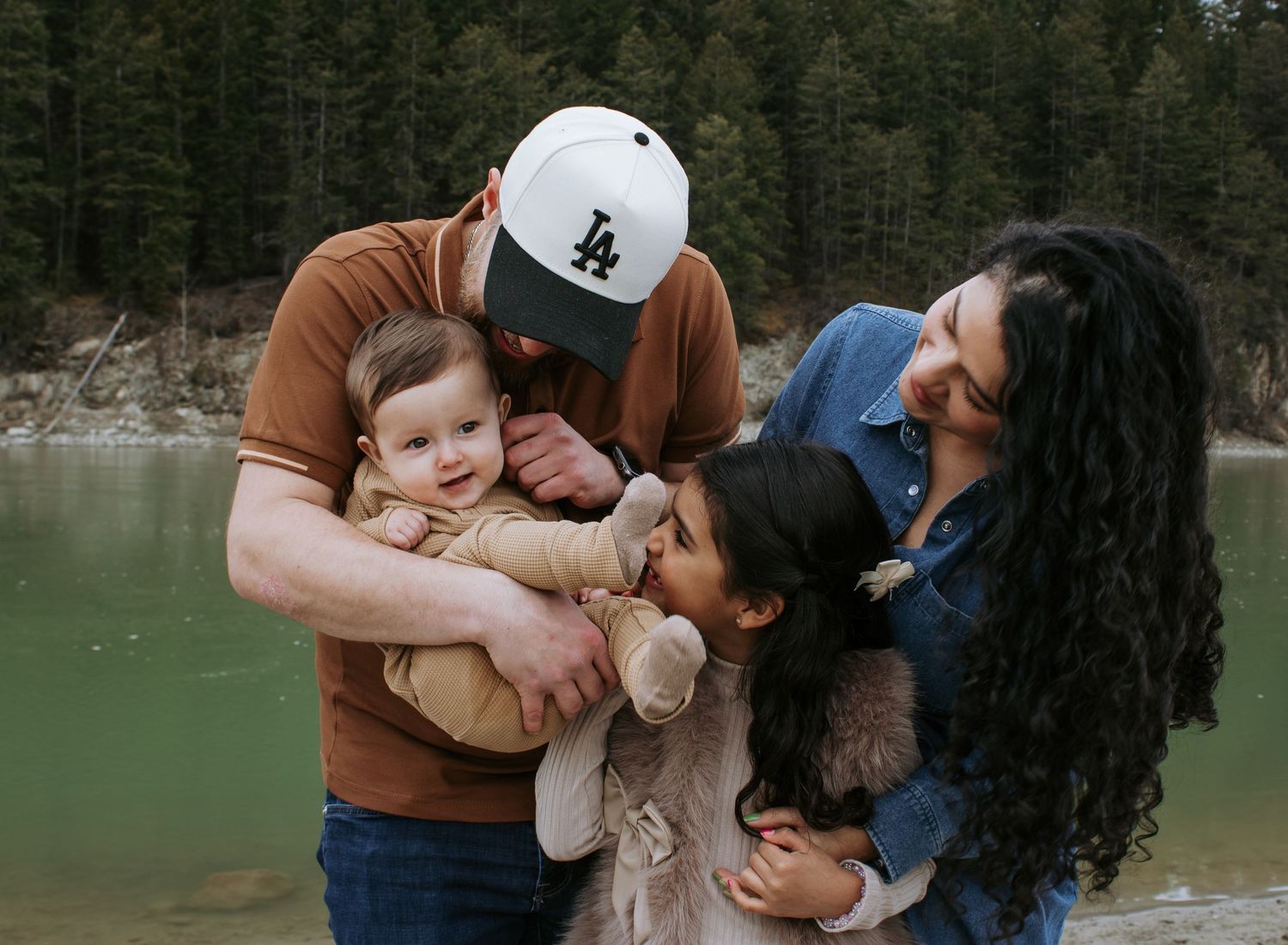 Happy family with two children smiling together near a scenic lake surrounded by trees.