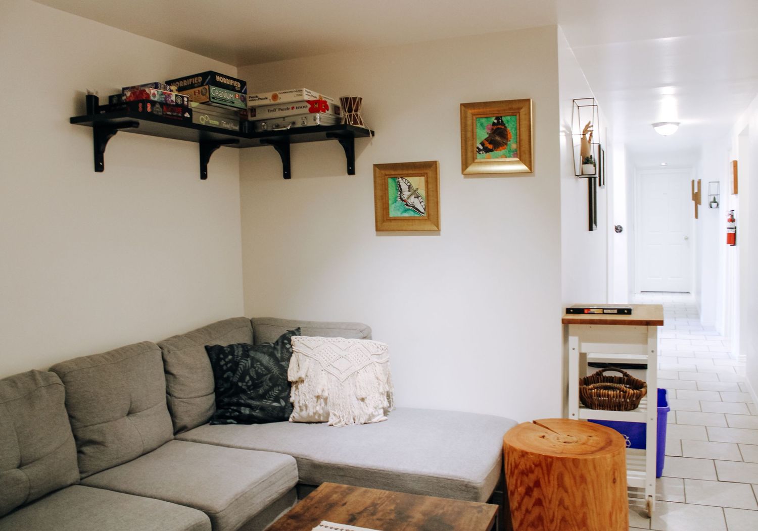 Long living room with grey couch, wooden accents, and wall-mounted shelving.