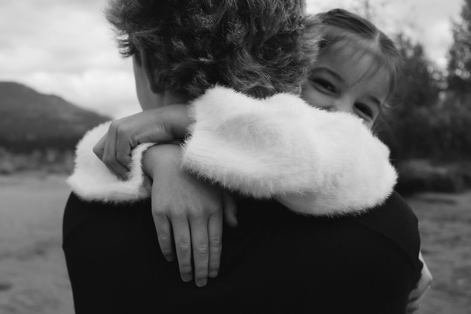 A tender embrace captured in black and white against a mountain landscape backdrop.