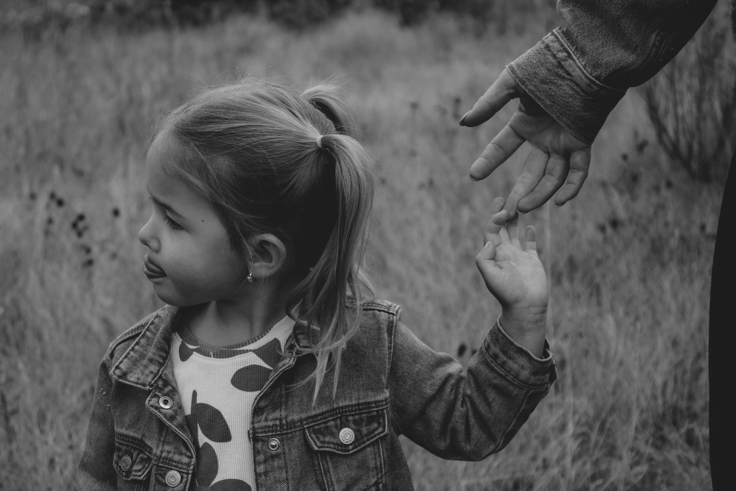 A close-up black and white image of a small hand reaching up to hold an adult's hand.