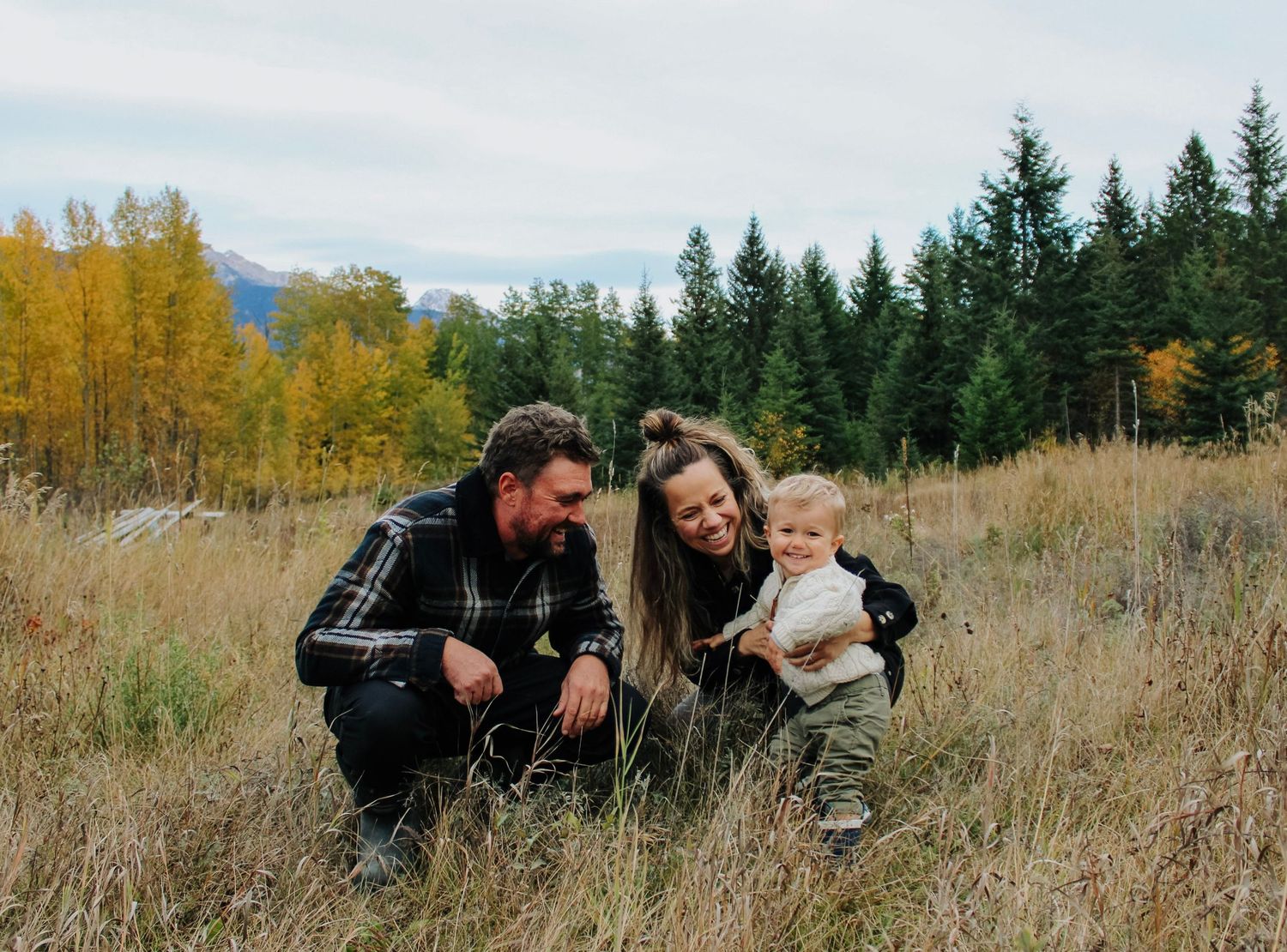 Family photo session in autumn field with mountains and golden trees in background.