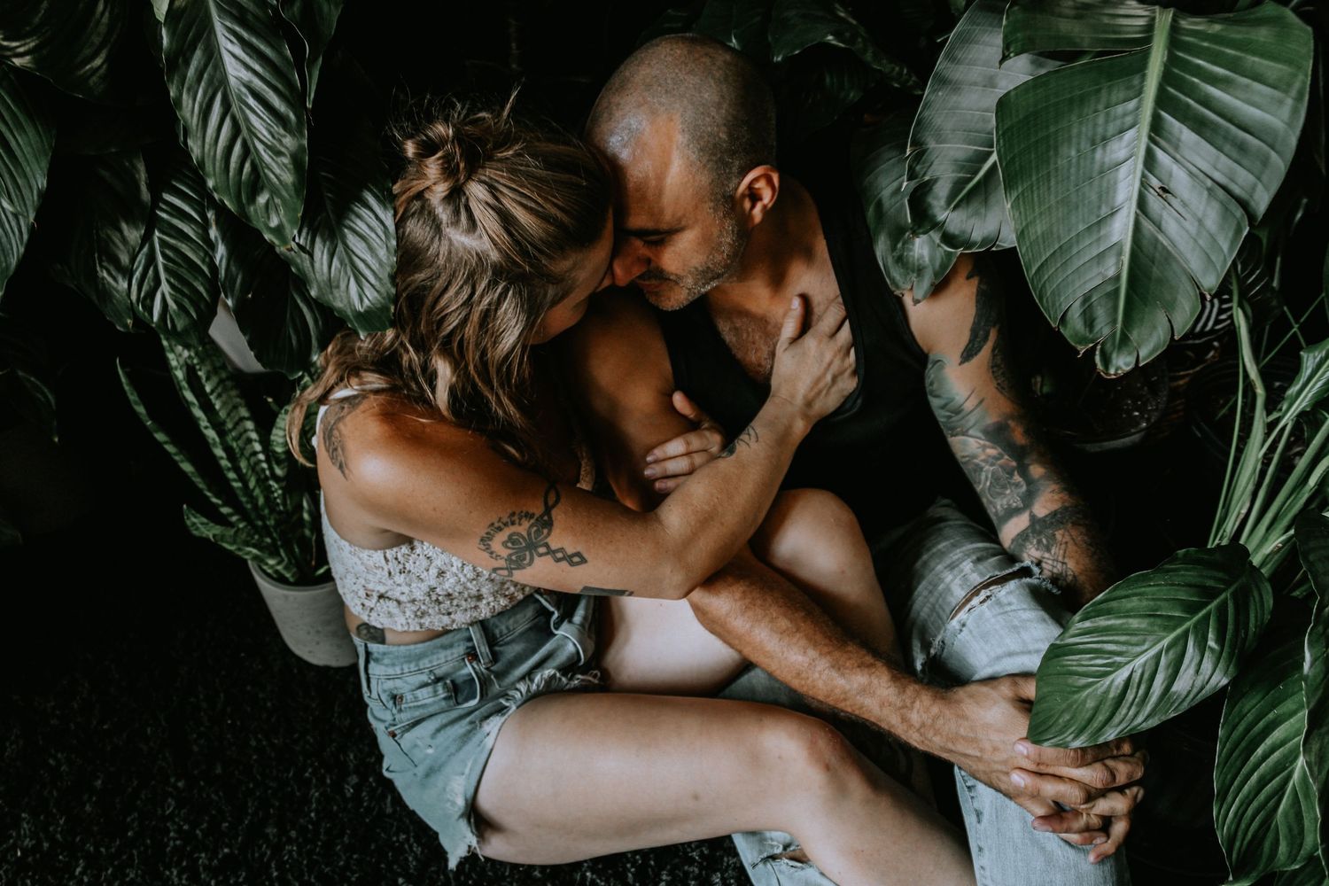 Intimate couple's portrait session with tropical plants and moody lighting.