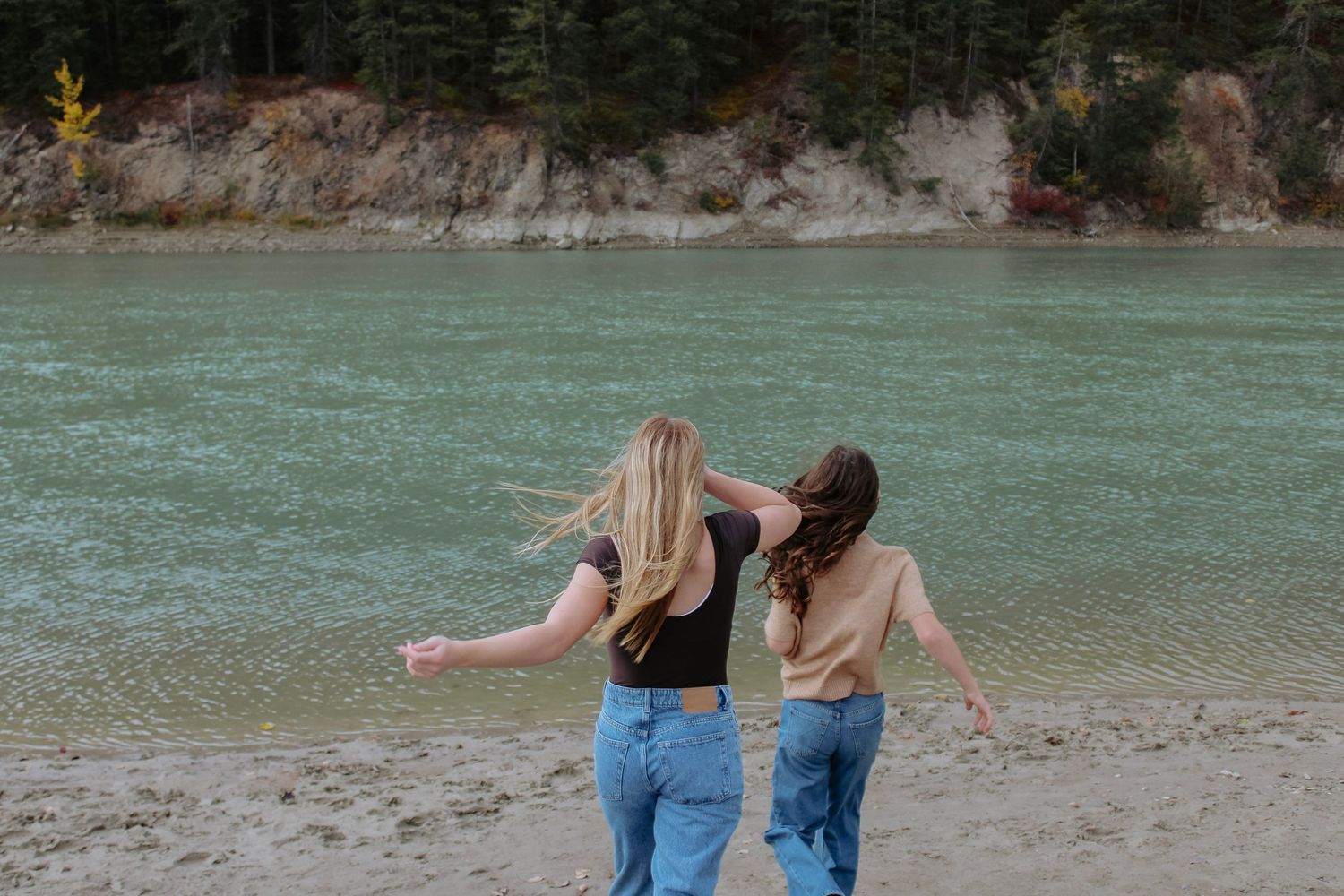 People walking along shoreline with turquoise water and mountain landscape.
