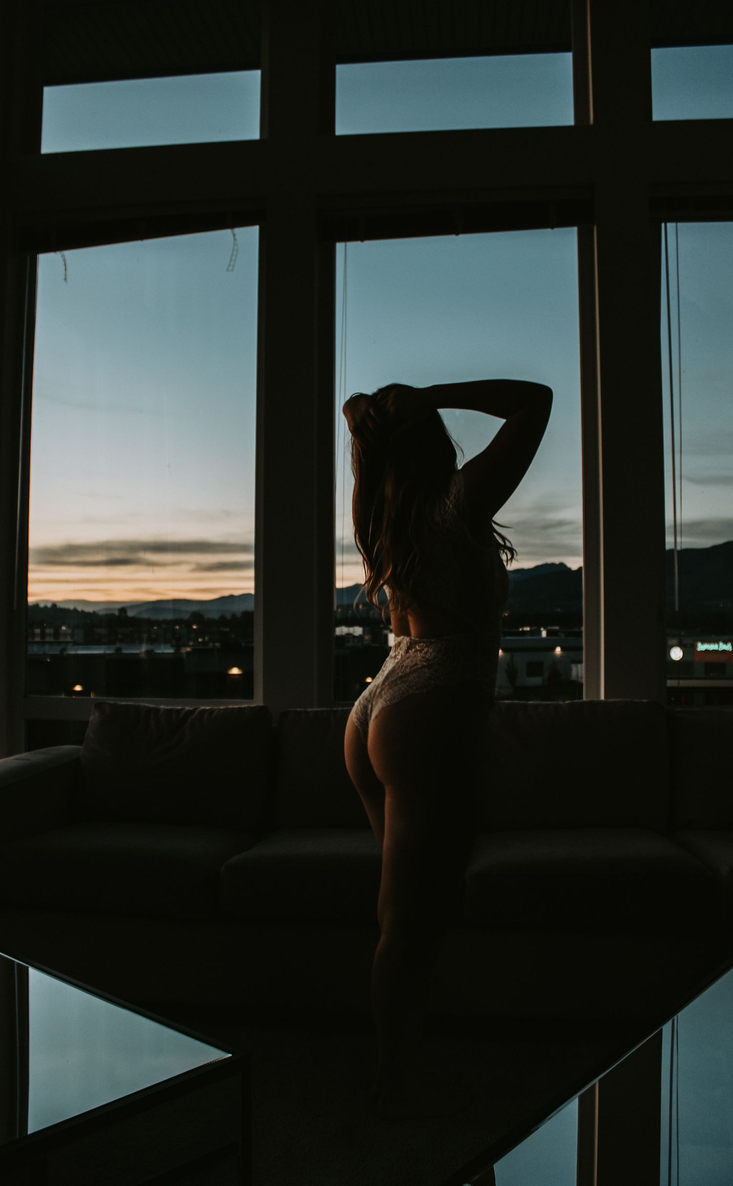 A silhouette stands by large windows during sunset in a moody indoor scene.