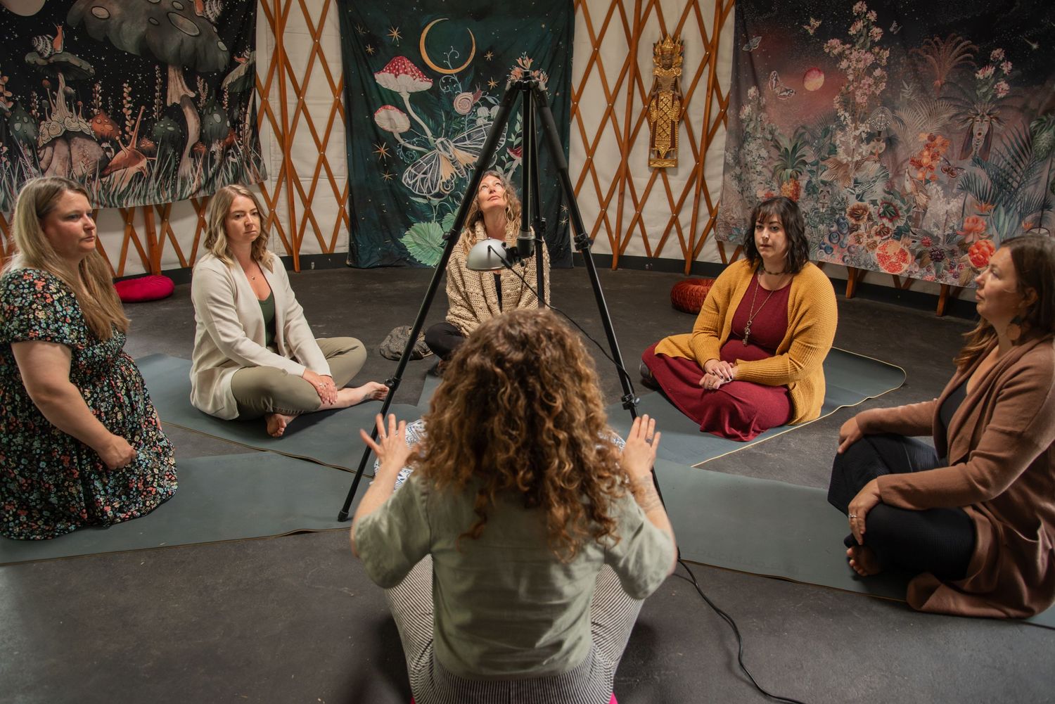 Women sitting in a circle during a meditation or wellness group session inside a decorated yurt space.