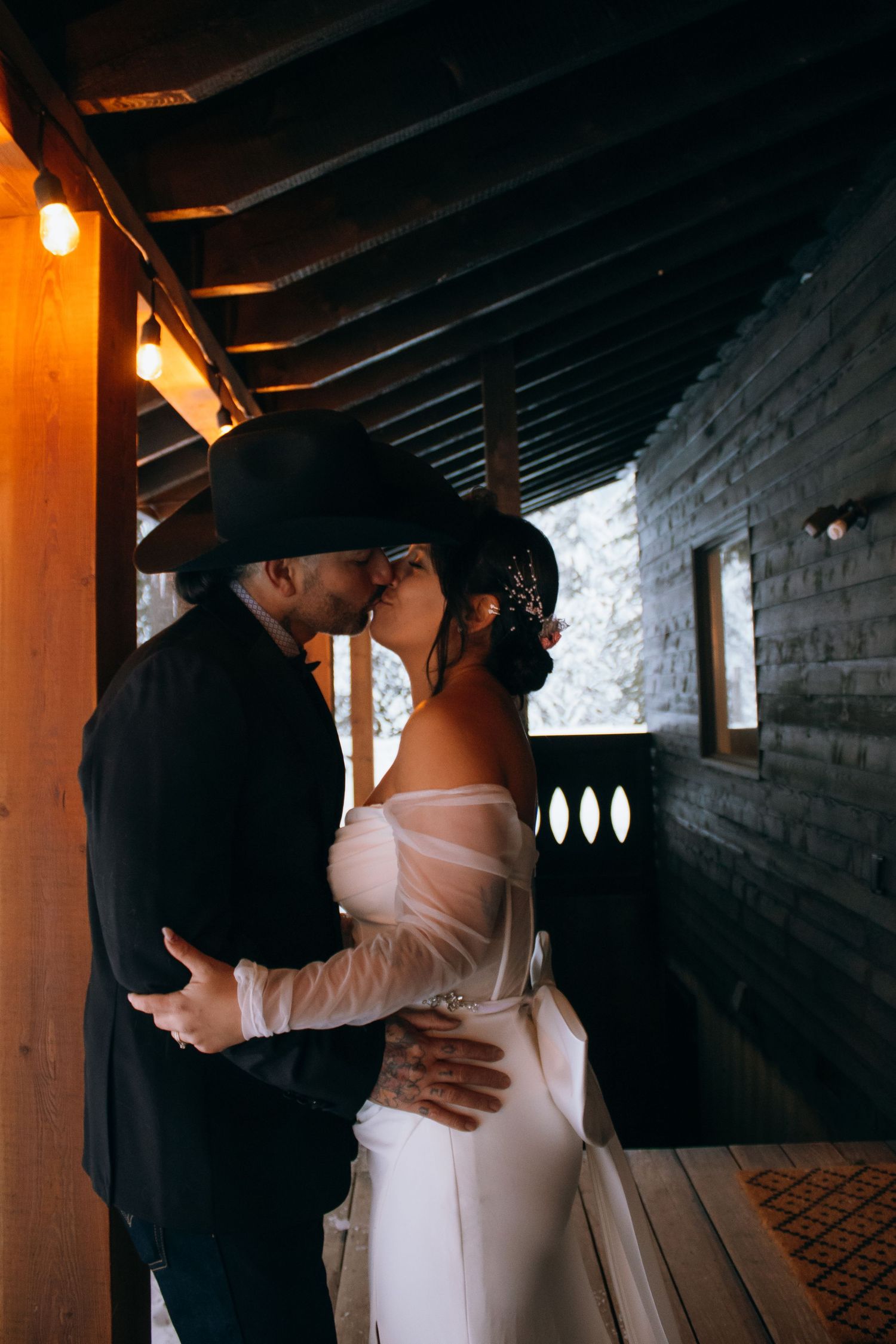 A romantic couple share an intimate moment in a rustic wooden hallway lit by warm lighting.