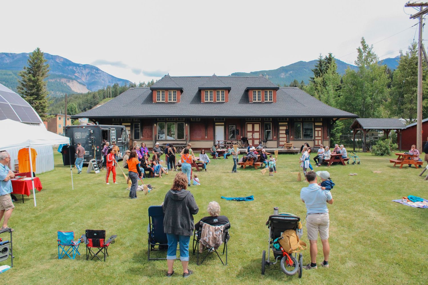 Outdoor community gathering on a green lawn in front of a lodge with mountain views on a sunny day.