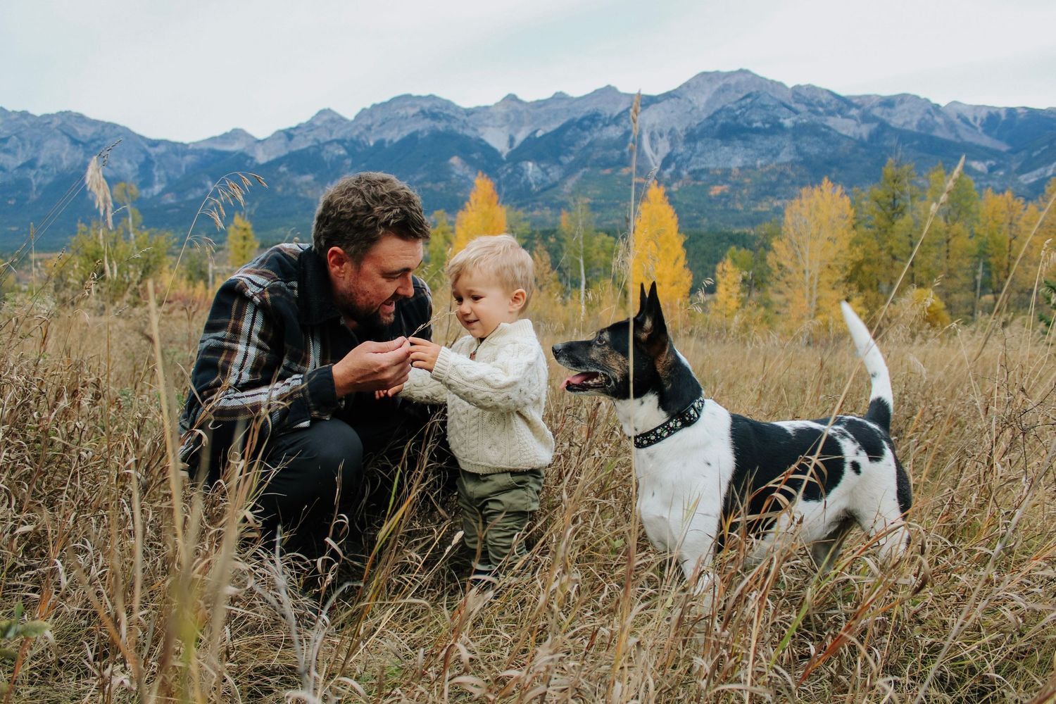 Outdoor family photoshoot with mountain backdrop and autumn foliage.