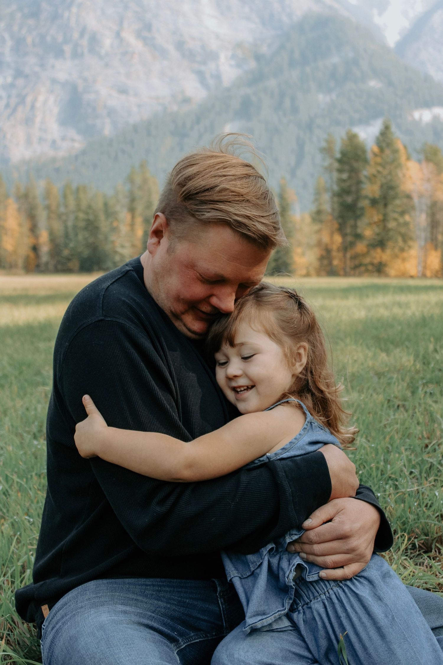 Candid moments of affection and laughter captured in a scenic mountain meadow setting.