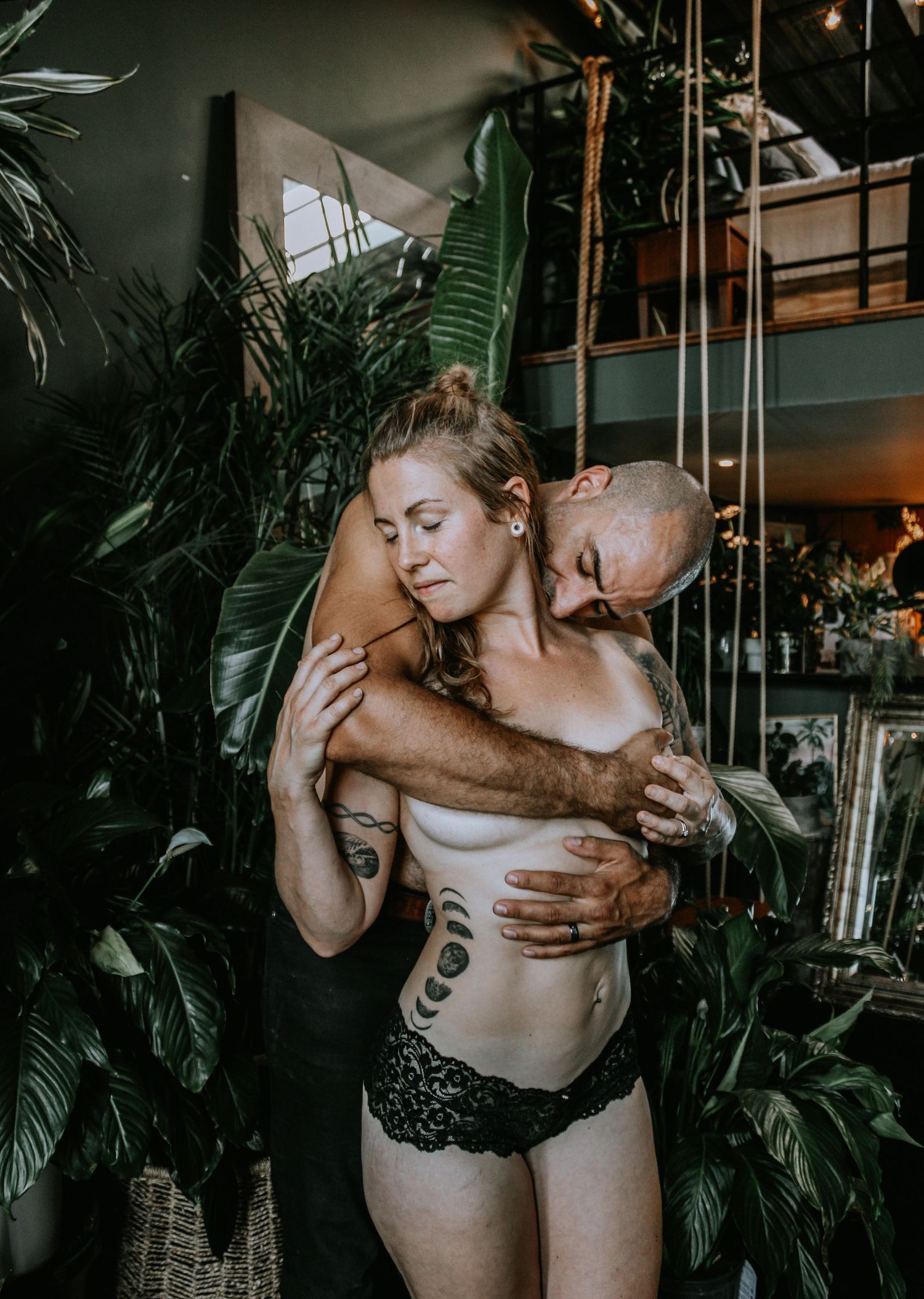 Artistic boudoir photoshoot featuring couple in intimate poses with tropical plant backdrop.