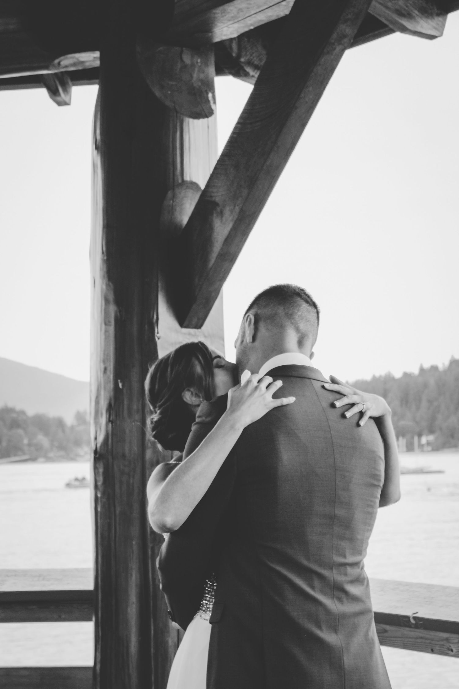 Black and white intimate moment captured under a wooden beam structure with mountain views.