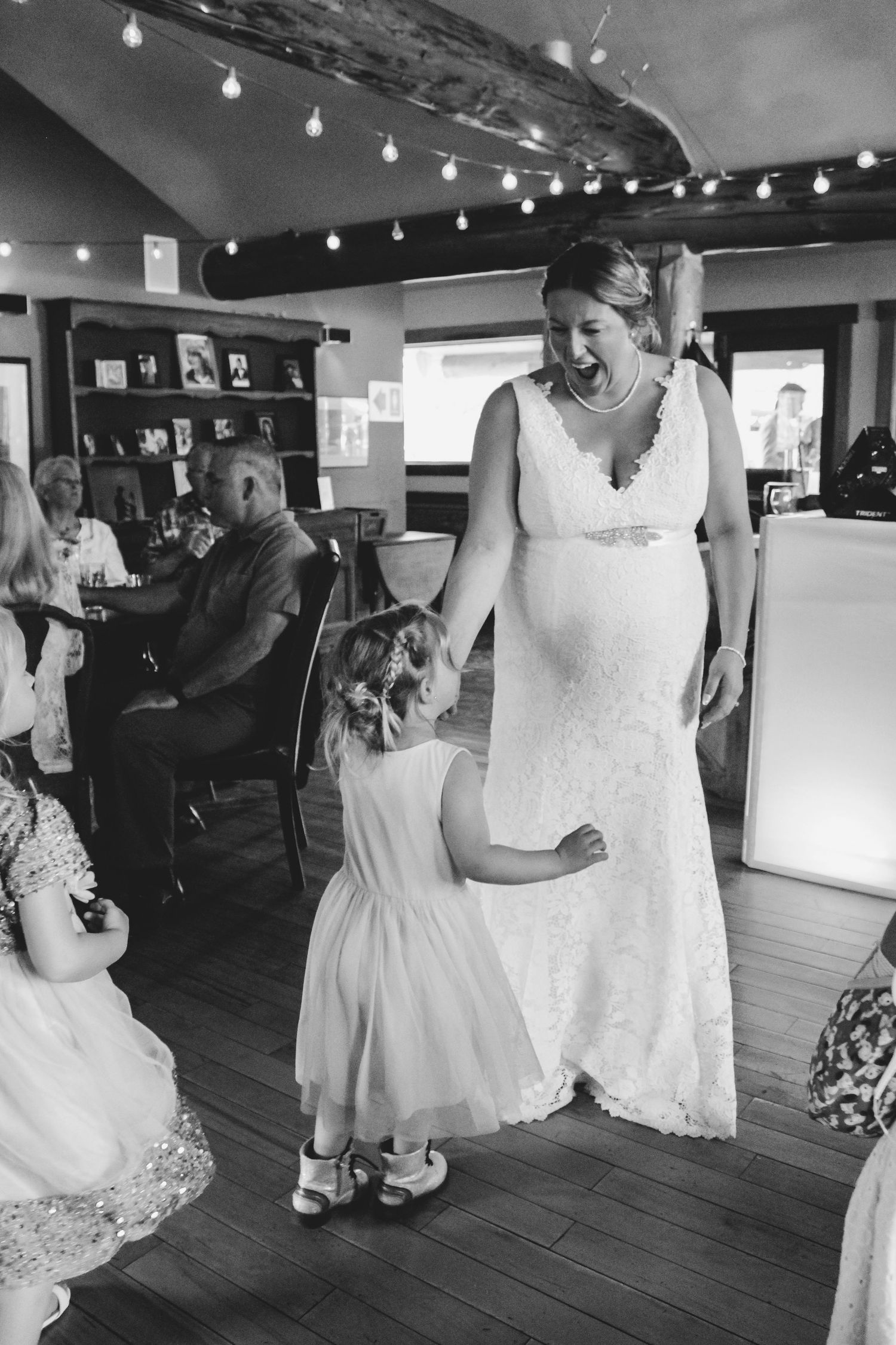 Wedding party members dancing and celebrating on a wooden dance floor under string lights.