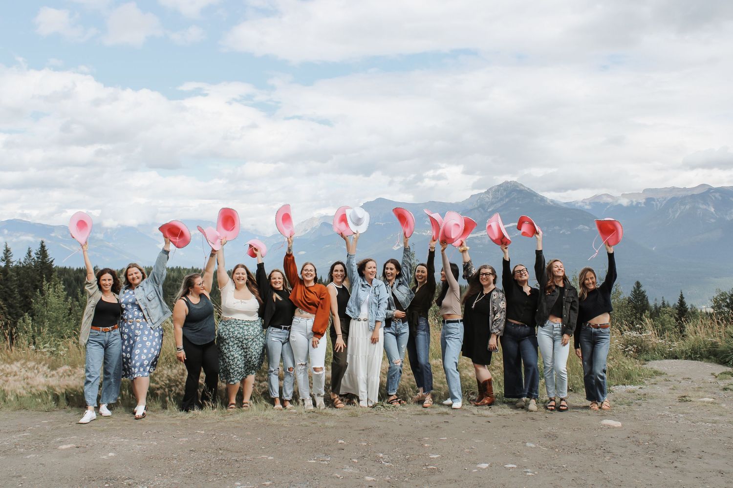 Group of women celebrating outdoors, raising red and white items, with mountains and cloudy sky in the background.