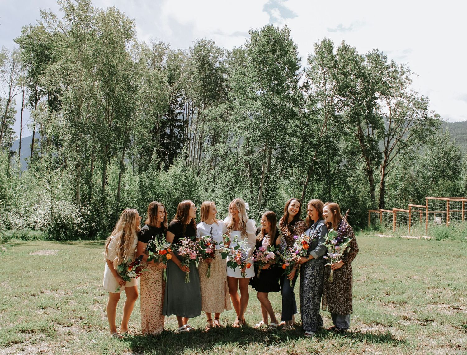 Group of bridesmaids holding colorful bouquets outdoors in a lush green meadow setting.