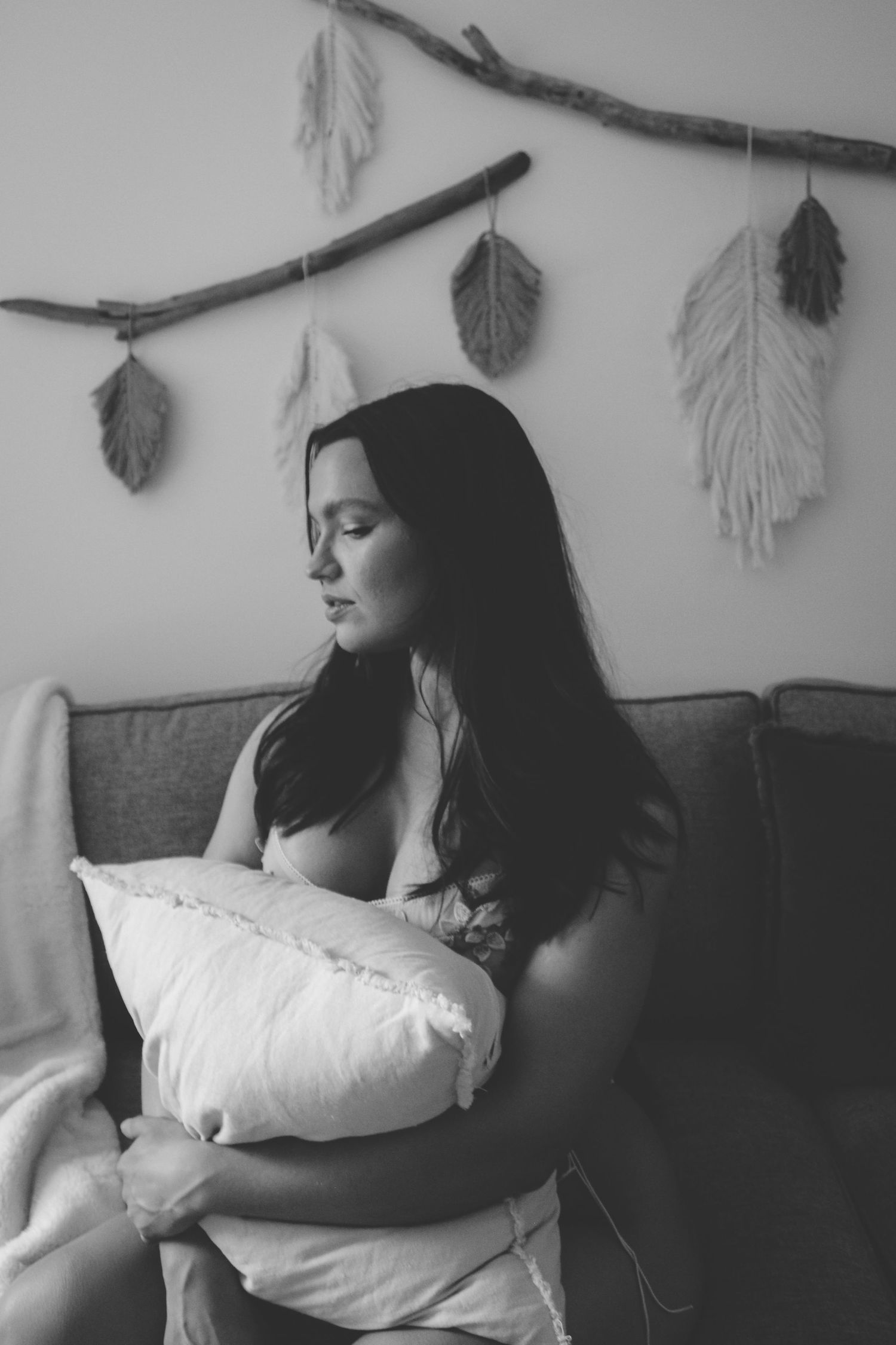 Black and white portrait of two people resting together with decorative feathers hanging above.