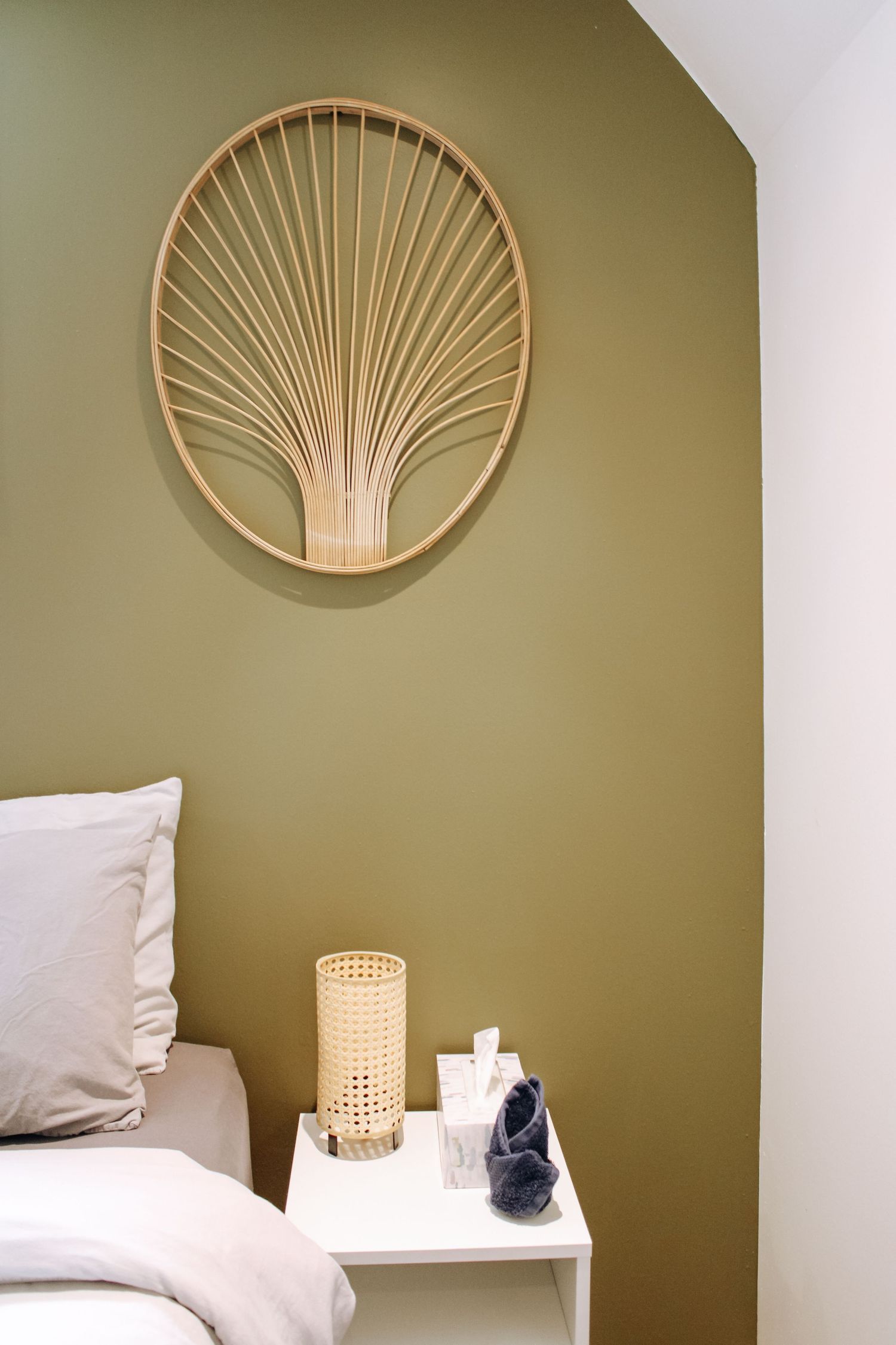 Modern bedroom with olive green accent wall featuring decorative sunburst wall art and bedside lamp.