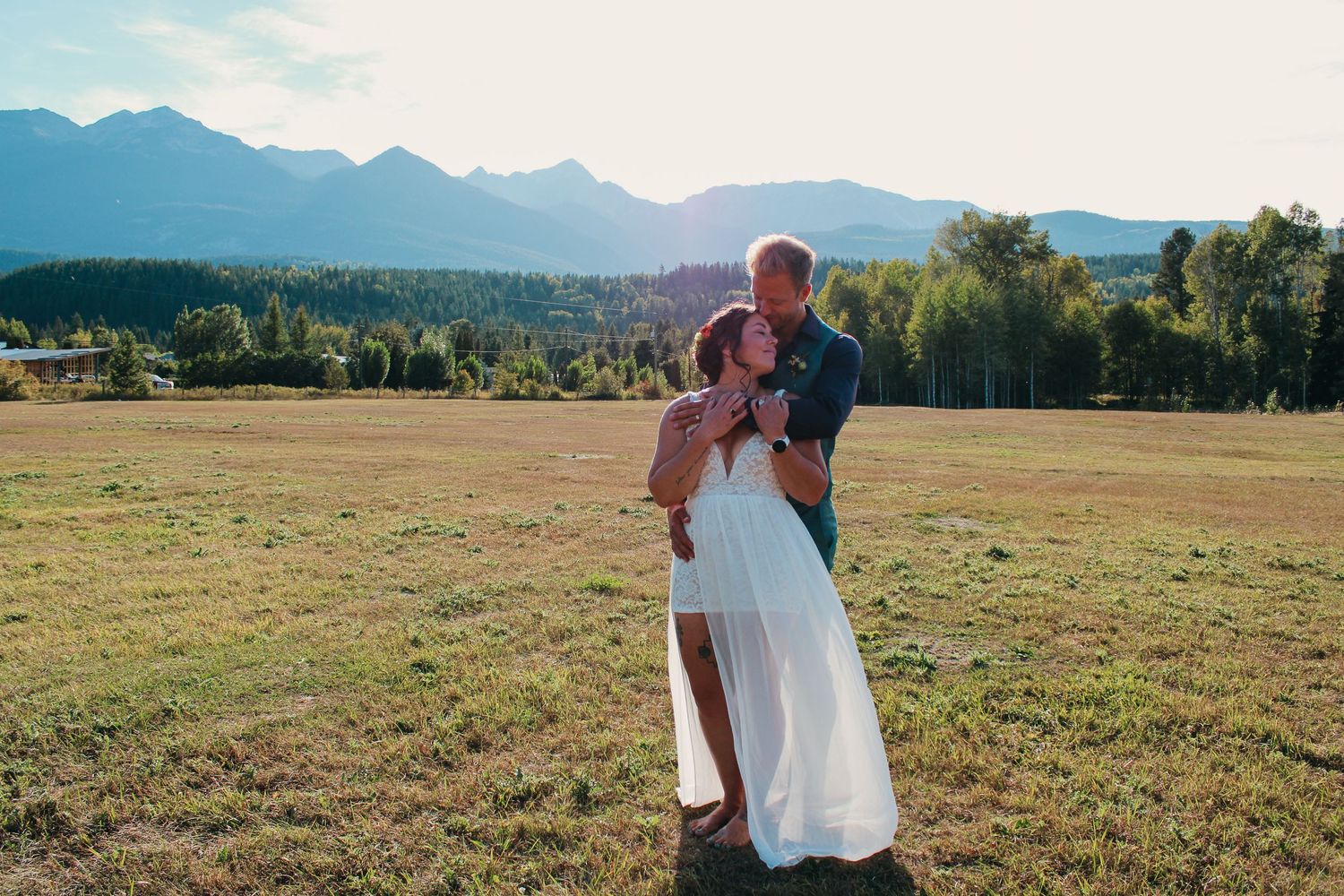 Couple sharing tender moments in an open field with mountains and blue skies.