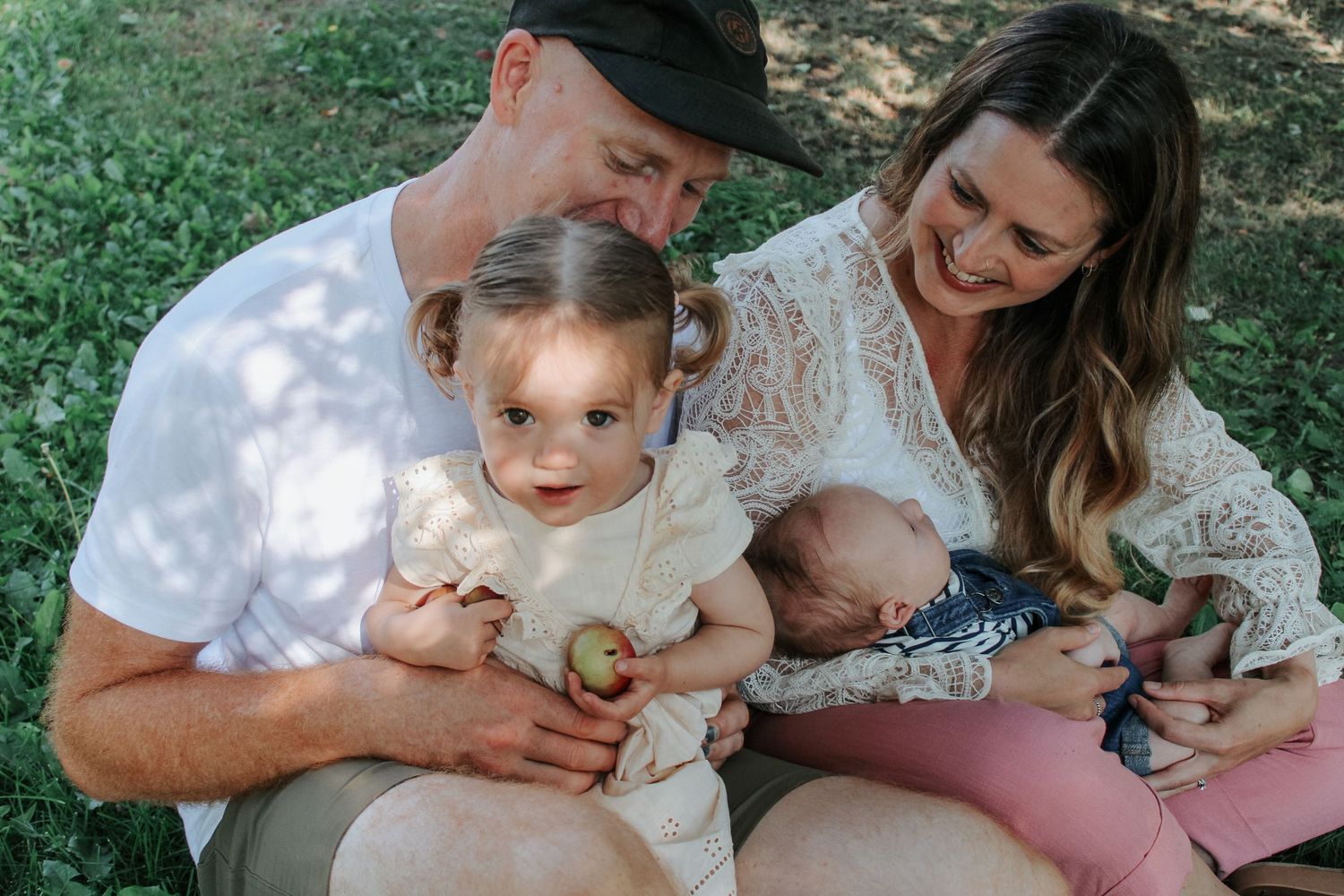 A family shares tender moments together on a sunny day in a grassy outdoor setting.