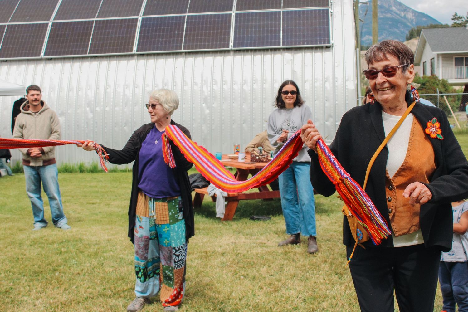 Two women holding a colorful ribbon at an outdoor solar panel ribbon-cutting ceremony celebration.