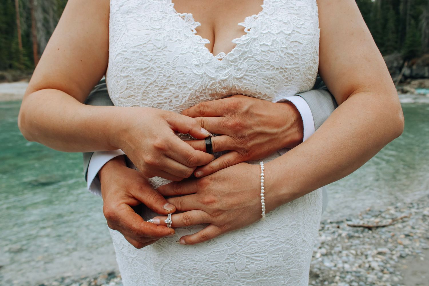 Close-up of hands with wedding rings against white lace dress.