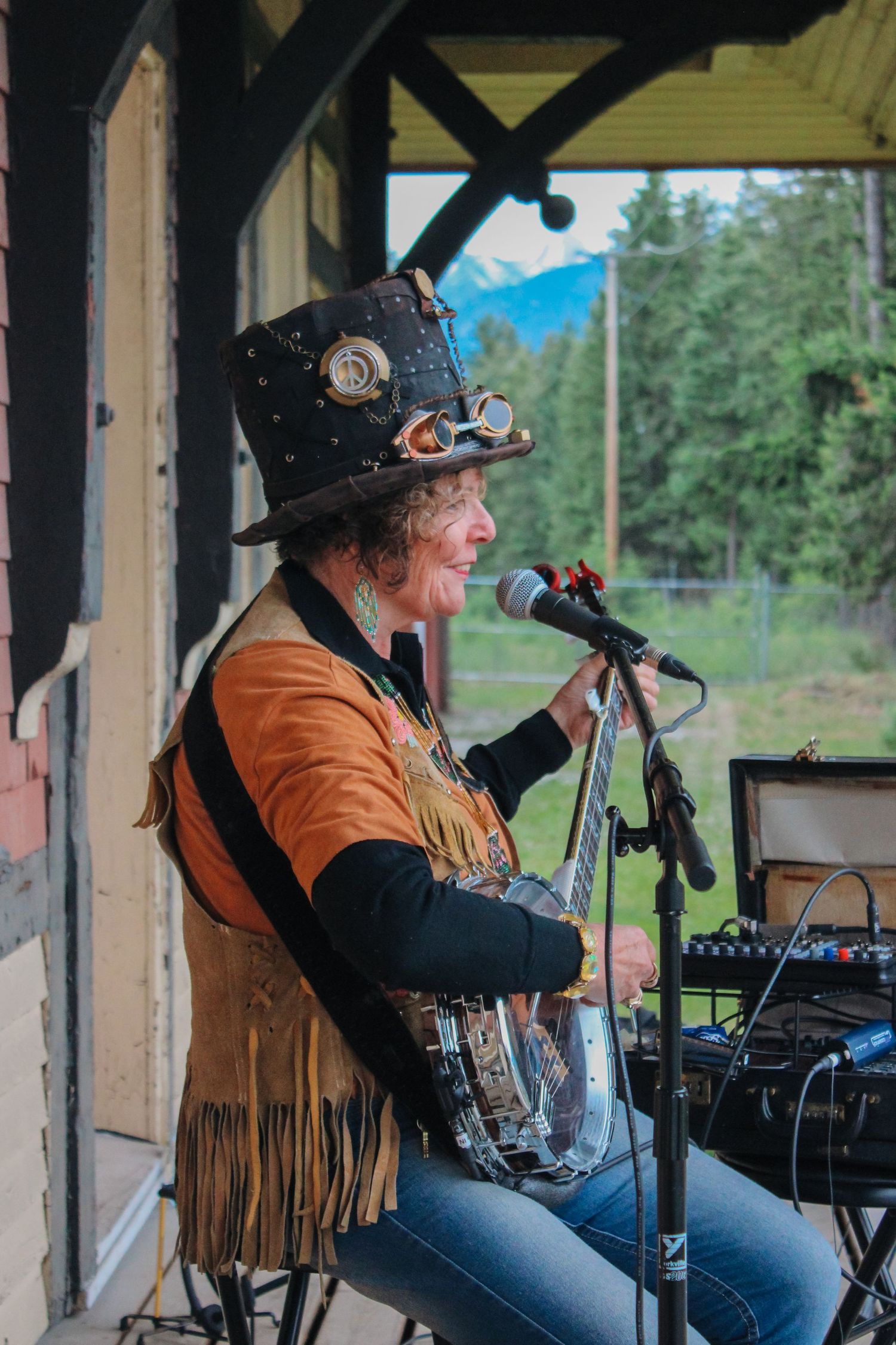 A steampunk performer in a decorated top hat with goggles sings into a microphone on an outdoor stage.