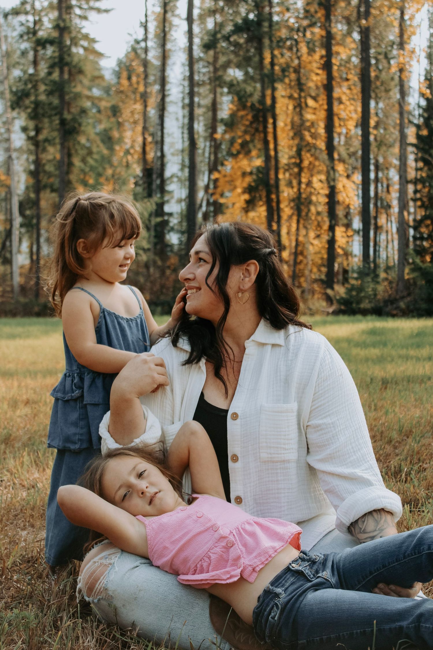 Tender family moments shared while relaxing in a sunlit meadow with evergreen trees.