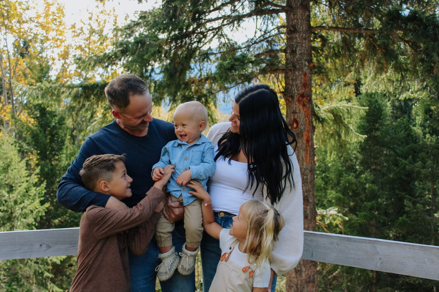 Family members share tender moments together in a sunlit forest setting.