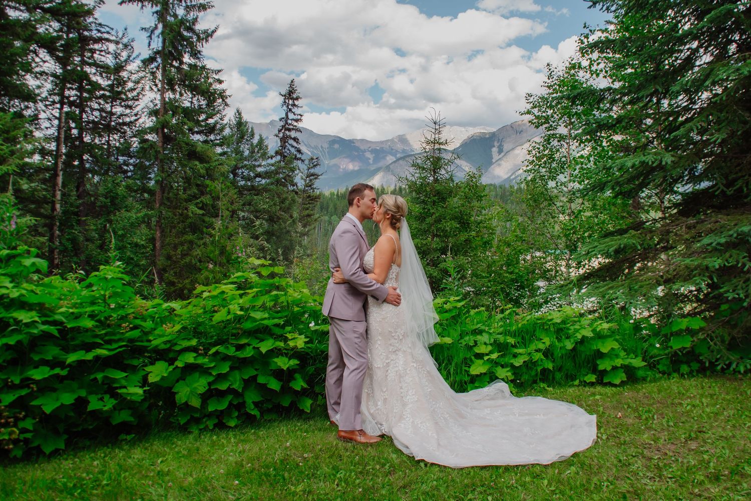 Bride and groom sharing a romantic kiss with stunning mountain backdrop on wedding day.