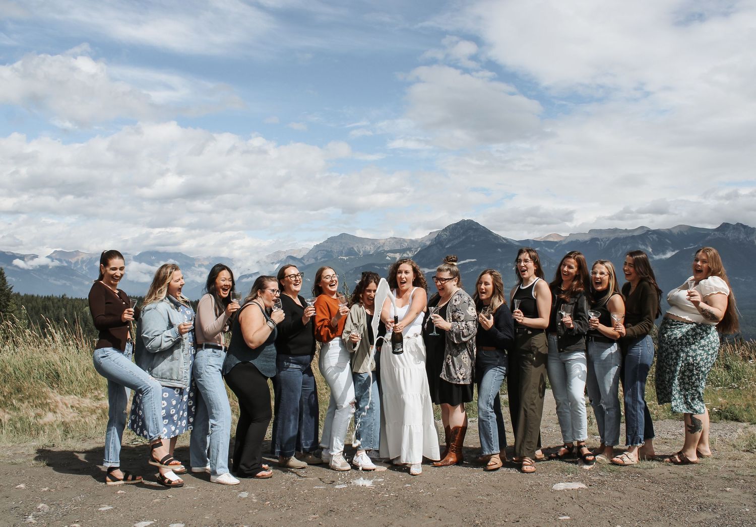 Group of women posing together outdoors with mountain landscape and cloudy sky in the background.