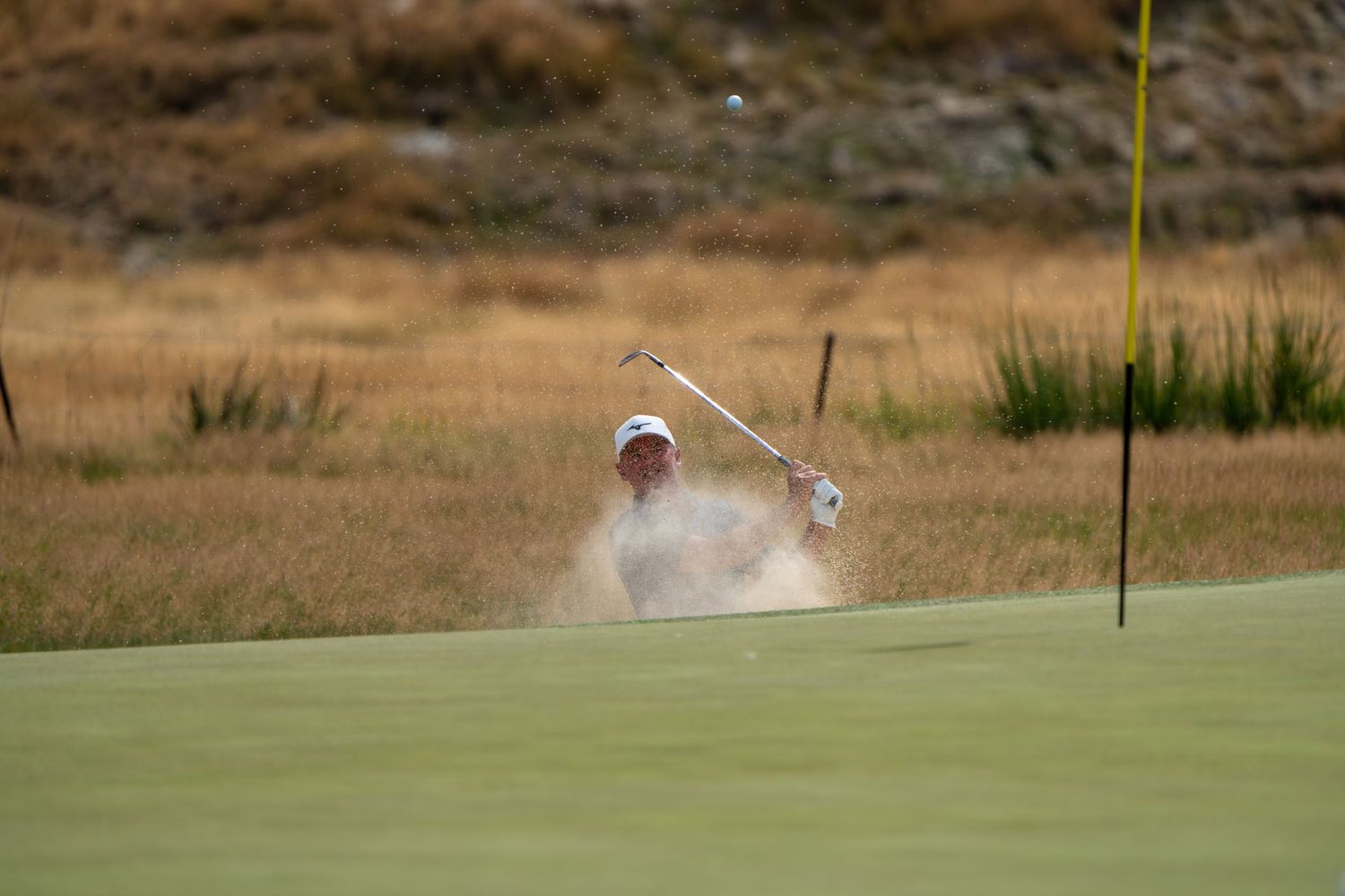 Golfer playing out of bunker to land his ball next to the pin.