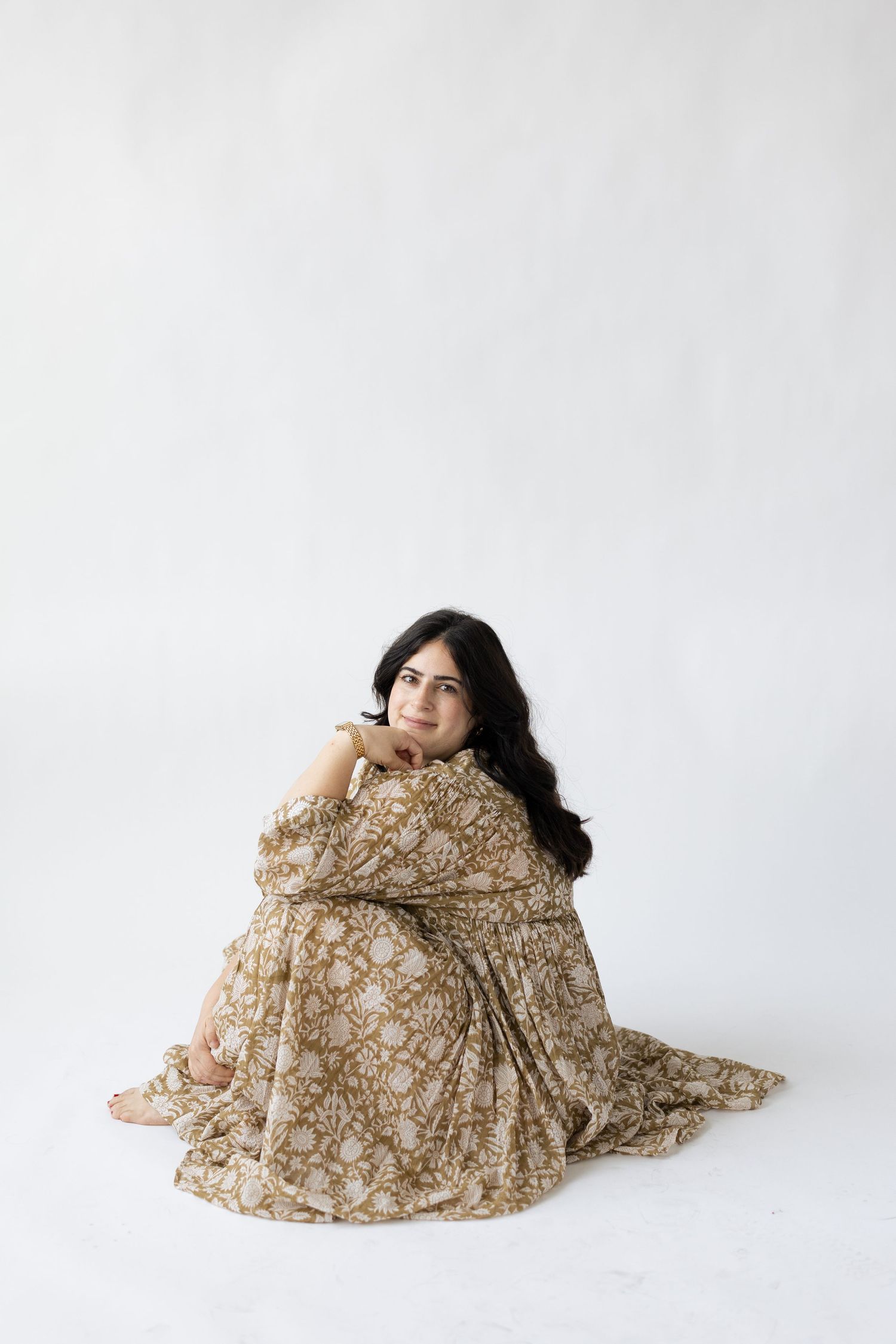 A person sits wrapped in a flowy beige floral dress against a white backdrop.