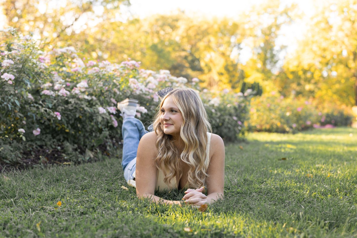 A person lies on grass during golden hour surrounded by flowering bushes.