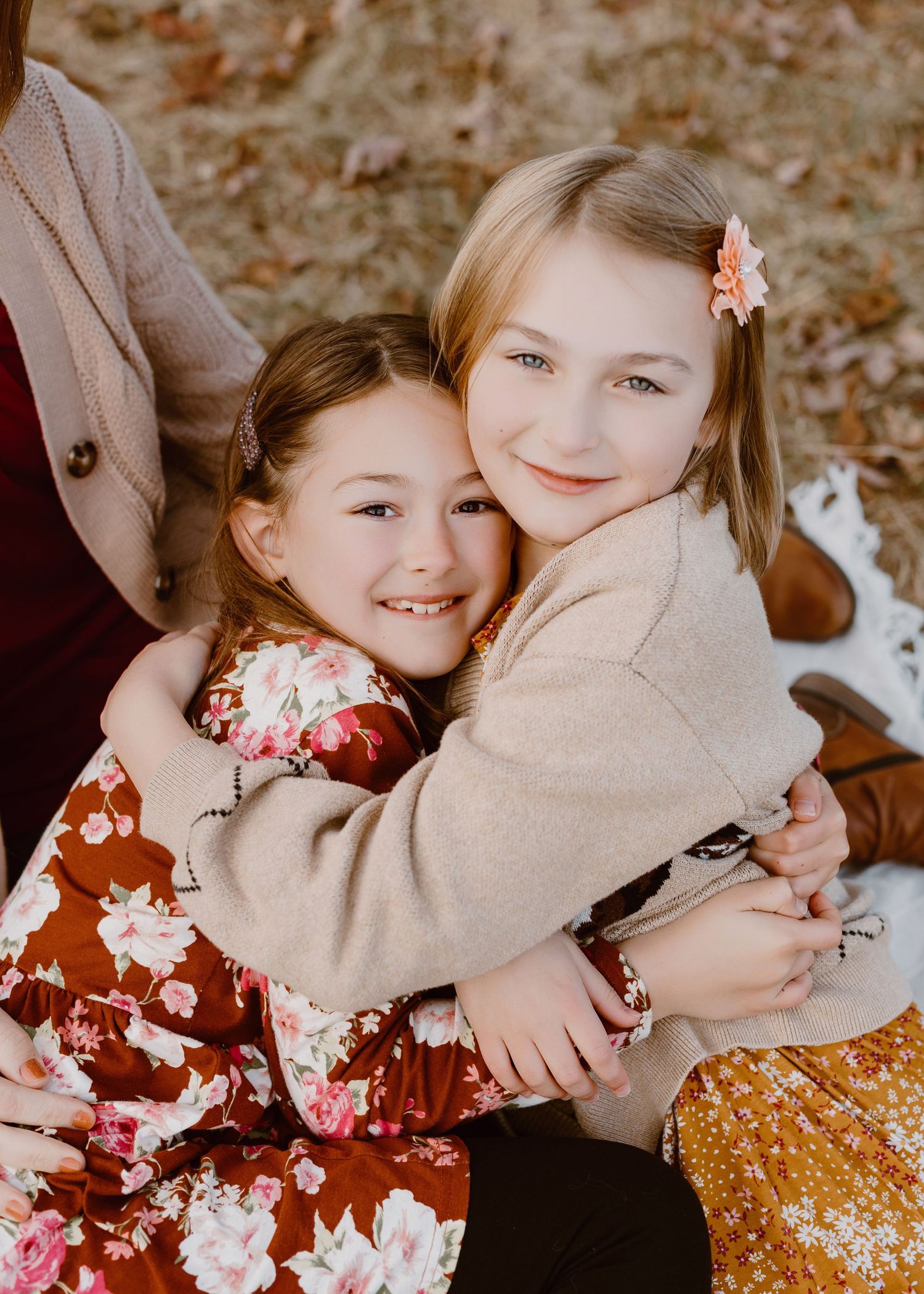 Two young sisters hugging and smiling outdoors during a fall family photo session.