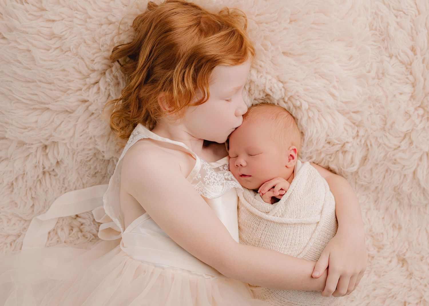 Tender moment of parent and newborn sleeping together on soft white textured backdrop.