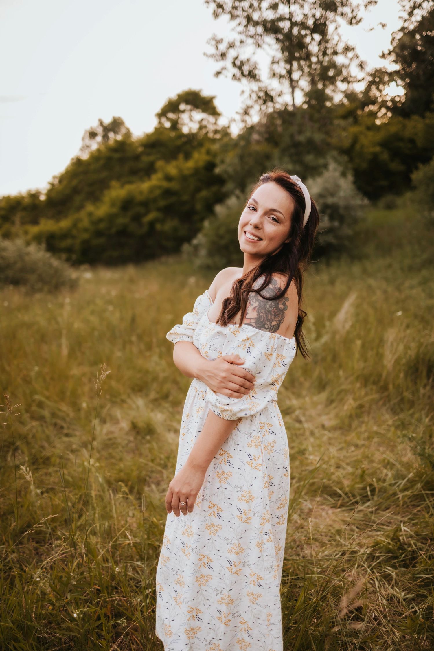 A person in a white floral dress dances and twirls joyfully in a sunlit meadow during golden hour. Oakland County, Michigan photographer