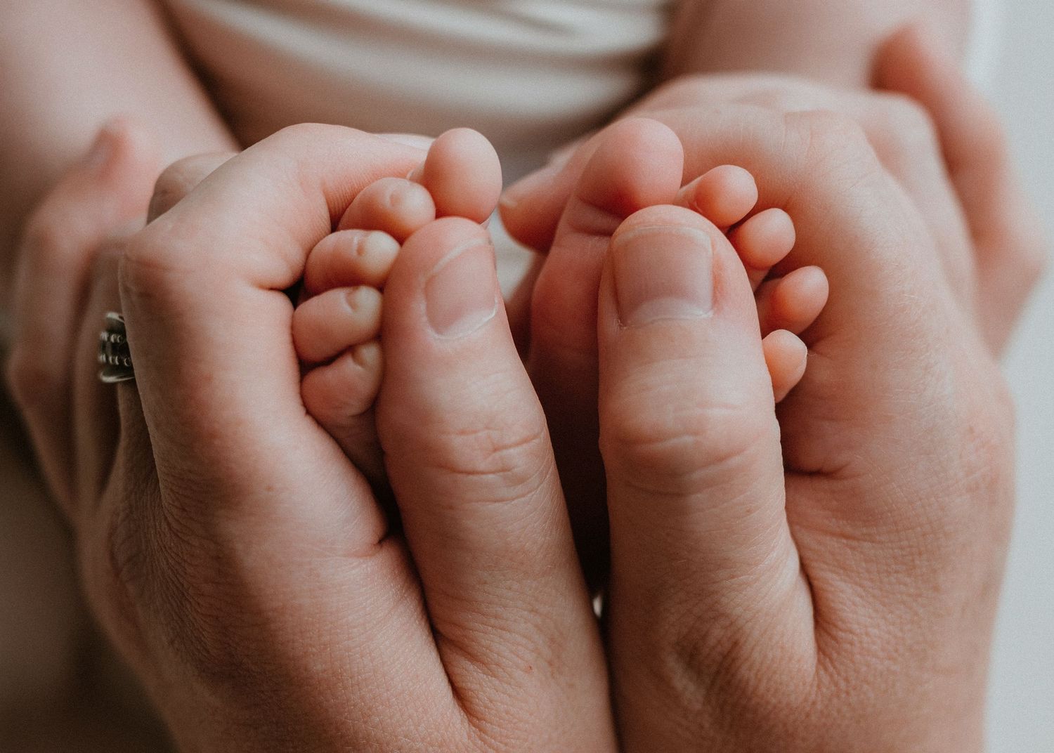 Adult hands gently cradling tiny newborn baby feet, showcasing a tender and loving parental moment.